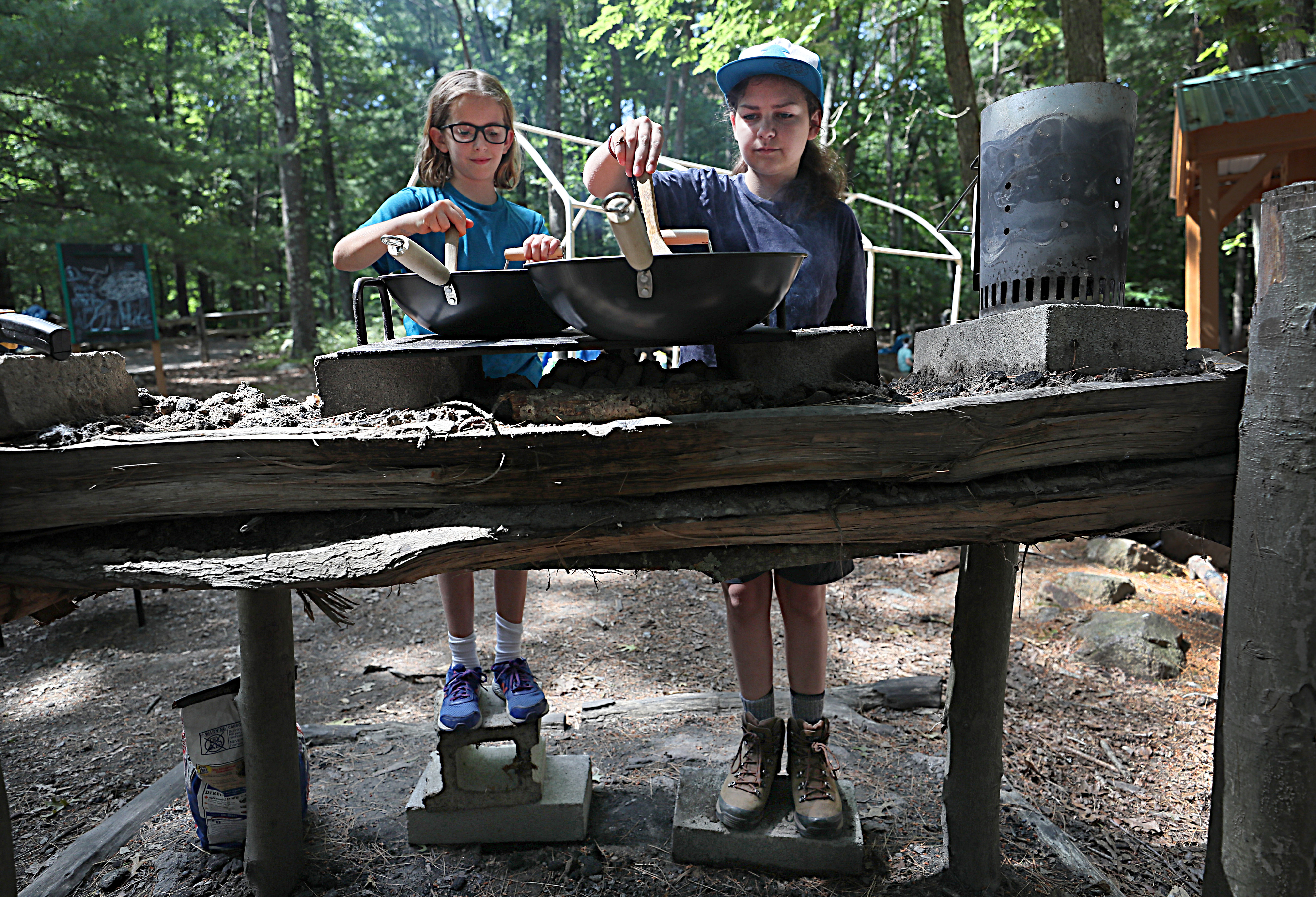 Rory Kilgore and Zoe Musante cooked vegetables on woks over a fire.