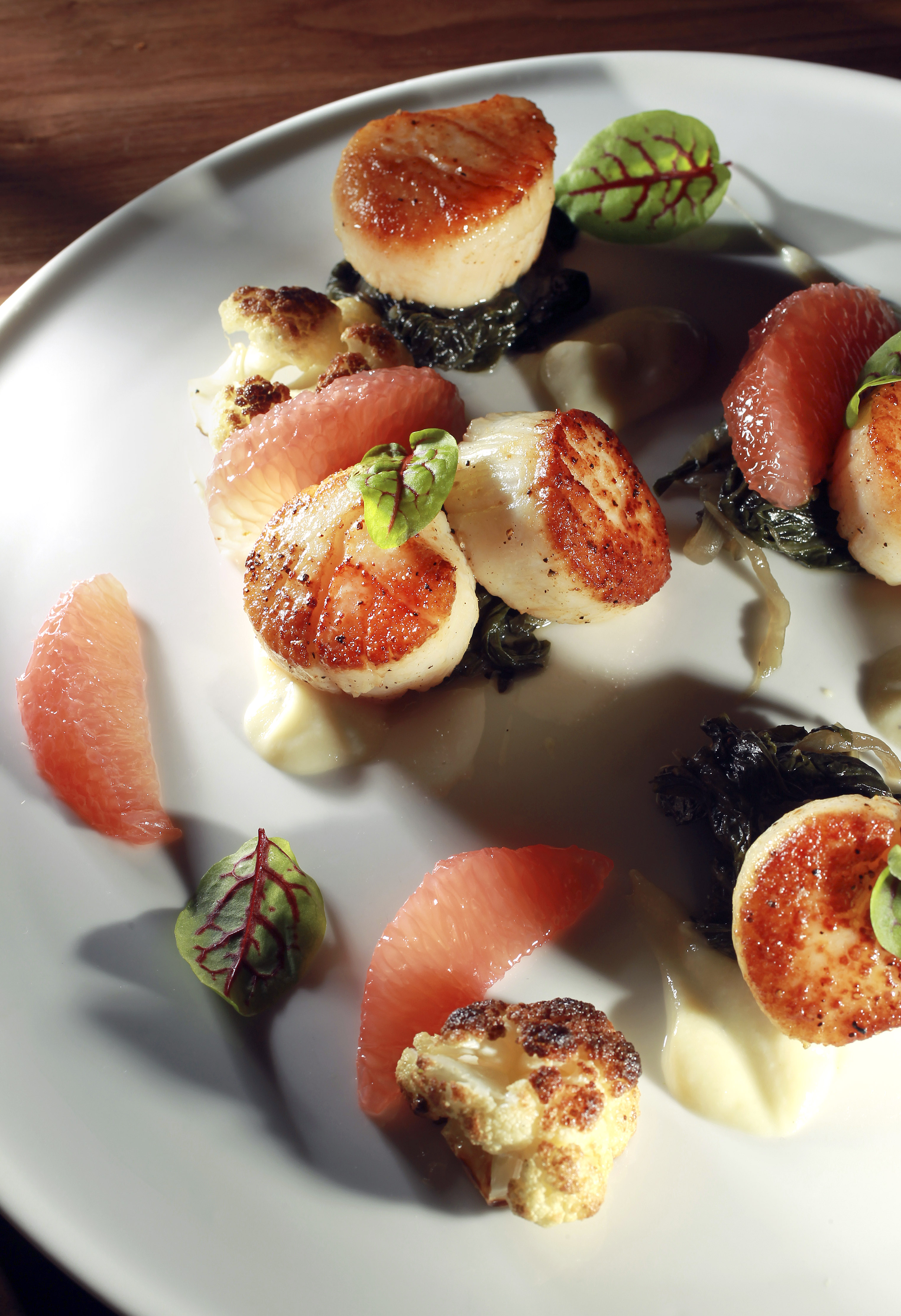 Seared scallops entree with cauliflower, grapefruit, Swiss chard, and bacon.
