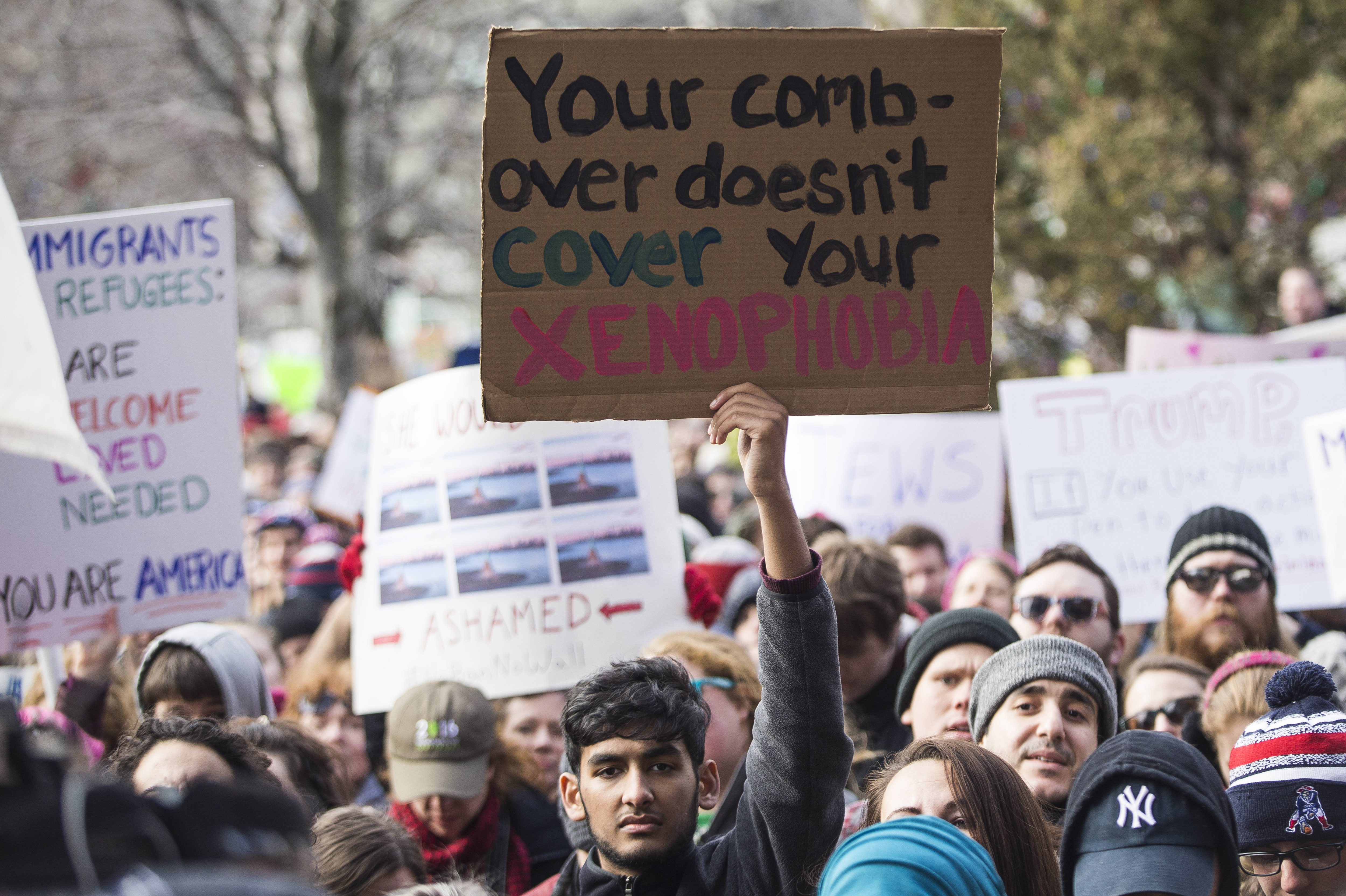 At least one sign took aim at both President Donald Trump’s immigration order and his hairstyle.