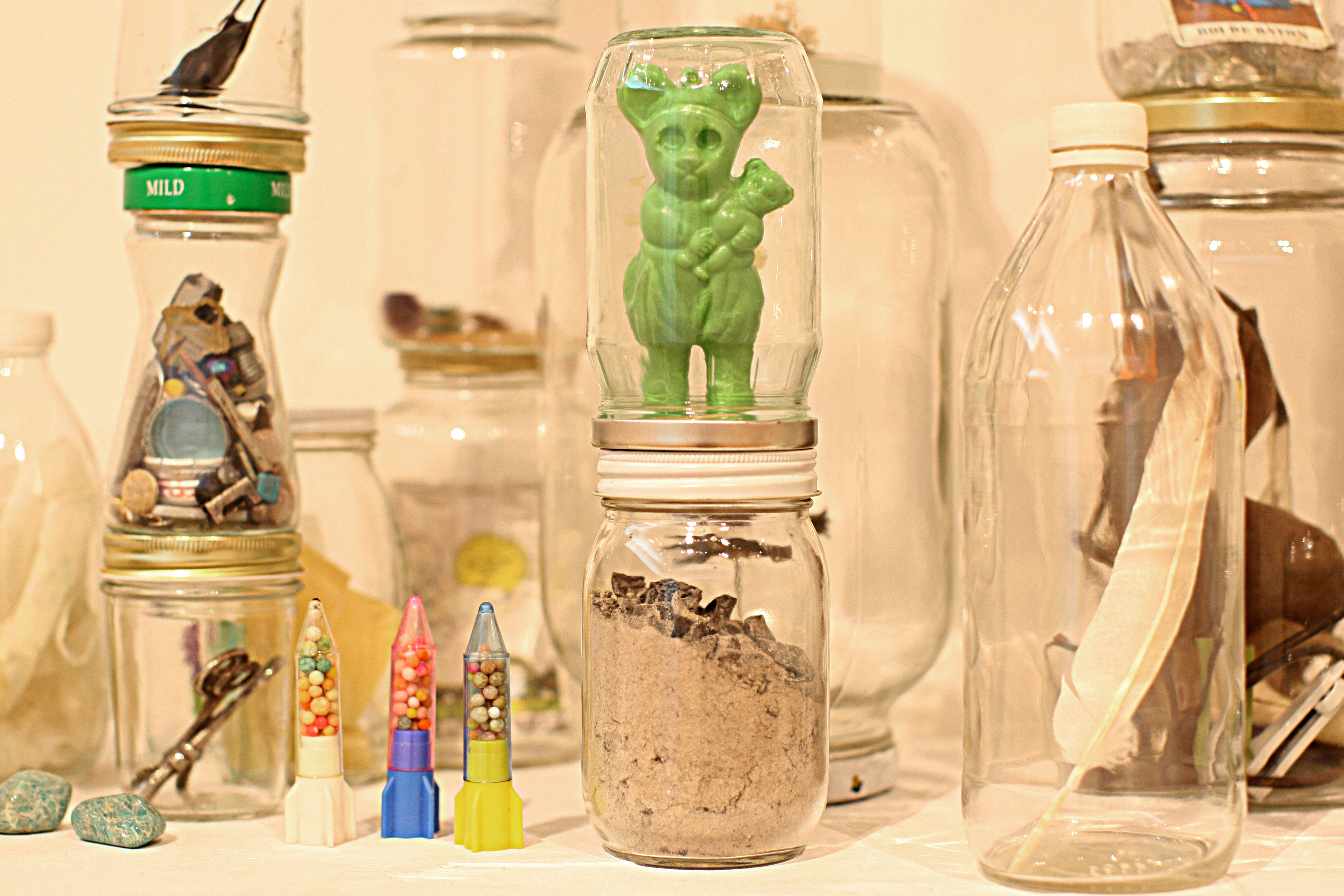 A Tony Feher sculpture of glass bottles and jars with lids, wooden table, and mixed media.