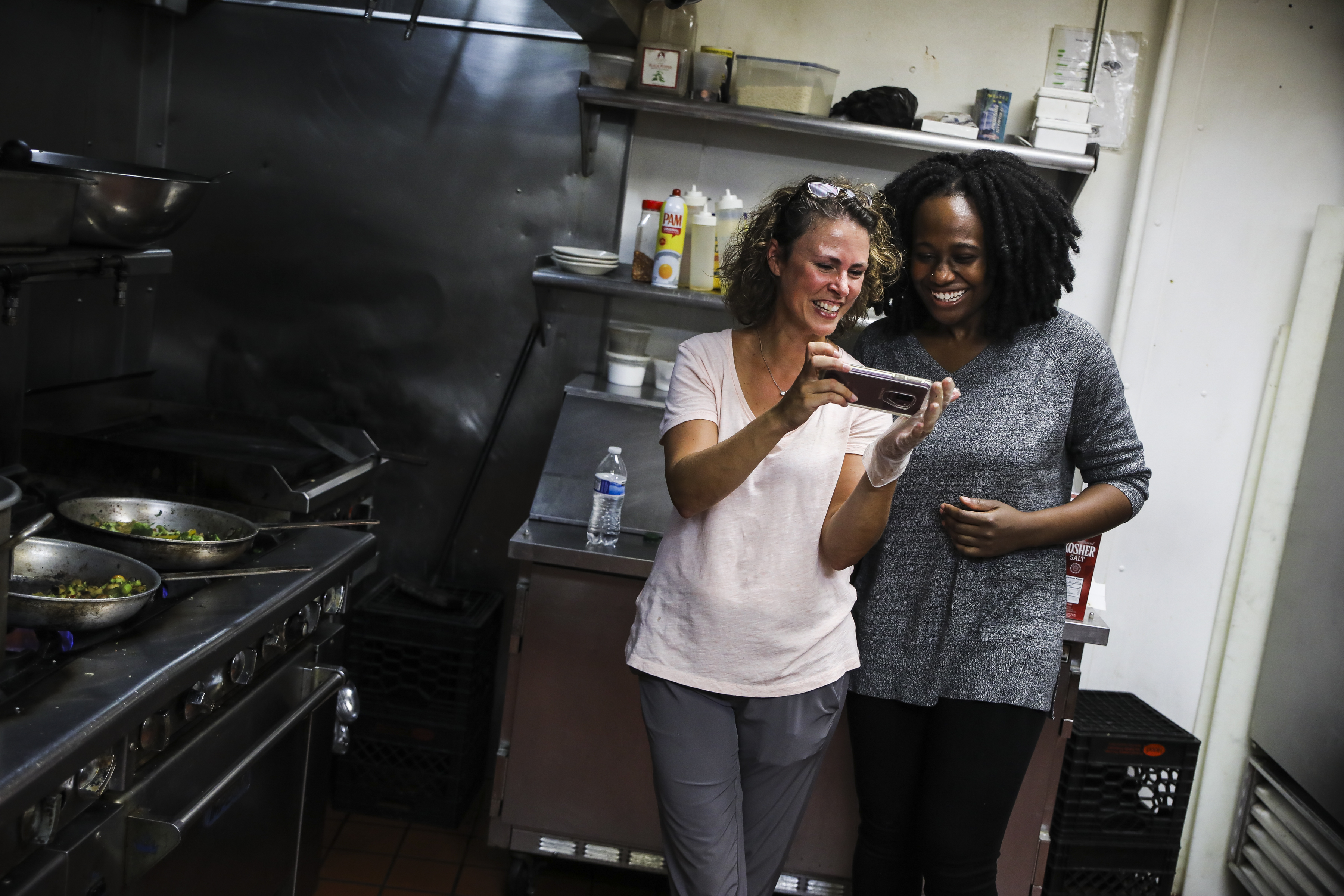 Sharry Tibbitt (left) and Nathanaelle Ibeziako looked at photos while taking a break from preparing trays of pasta primavera to be delivered to people along Methadone Mile.
