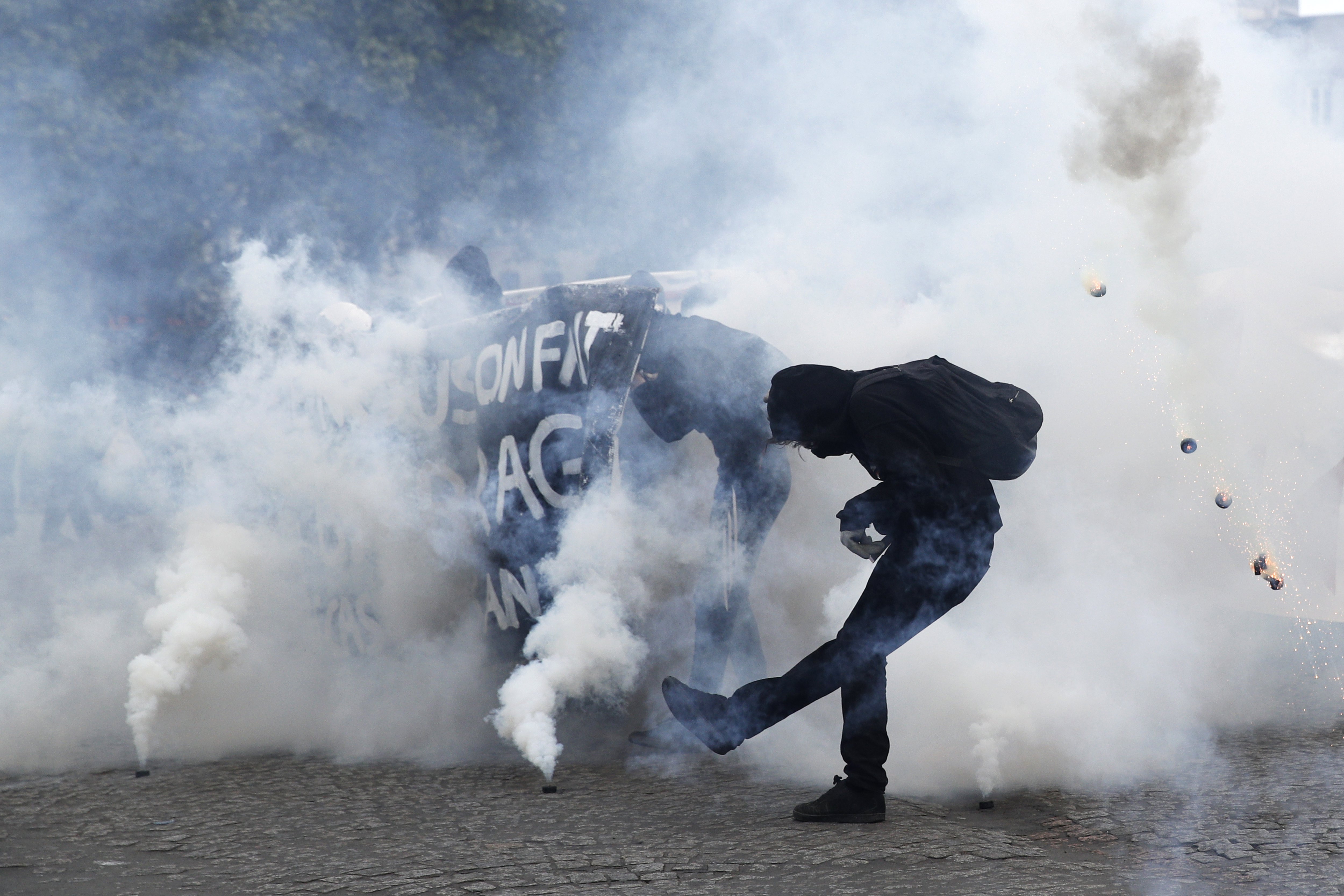 A protester kicked a tear gas container as clashes erupted between protesters and French police in Paris.