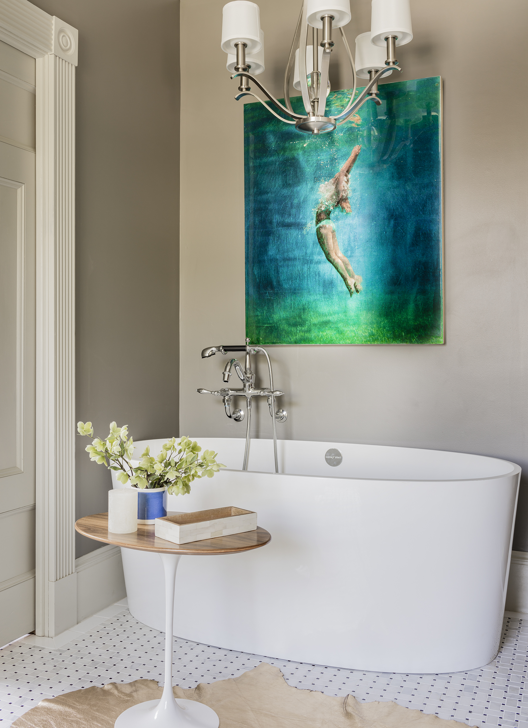 The wall-mounted Finial tub fixture by Kohler has a traditional silhouette that contrasts with the volcanic limestone bath by Victoria + Albert, a space-saving 60-inch tub designed for city living. Tall ceilings allowed for both artwork — Deep Angel II by Eric Zener, from Lanoue Gallery in SoWa — and the chandelier, a transitional-style fixture by Hinkley.