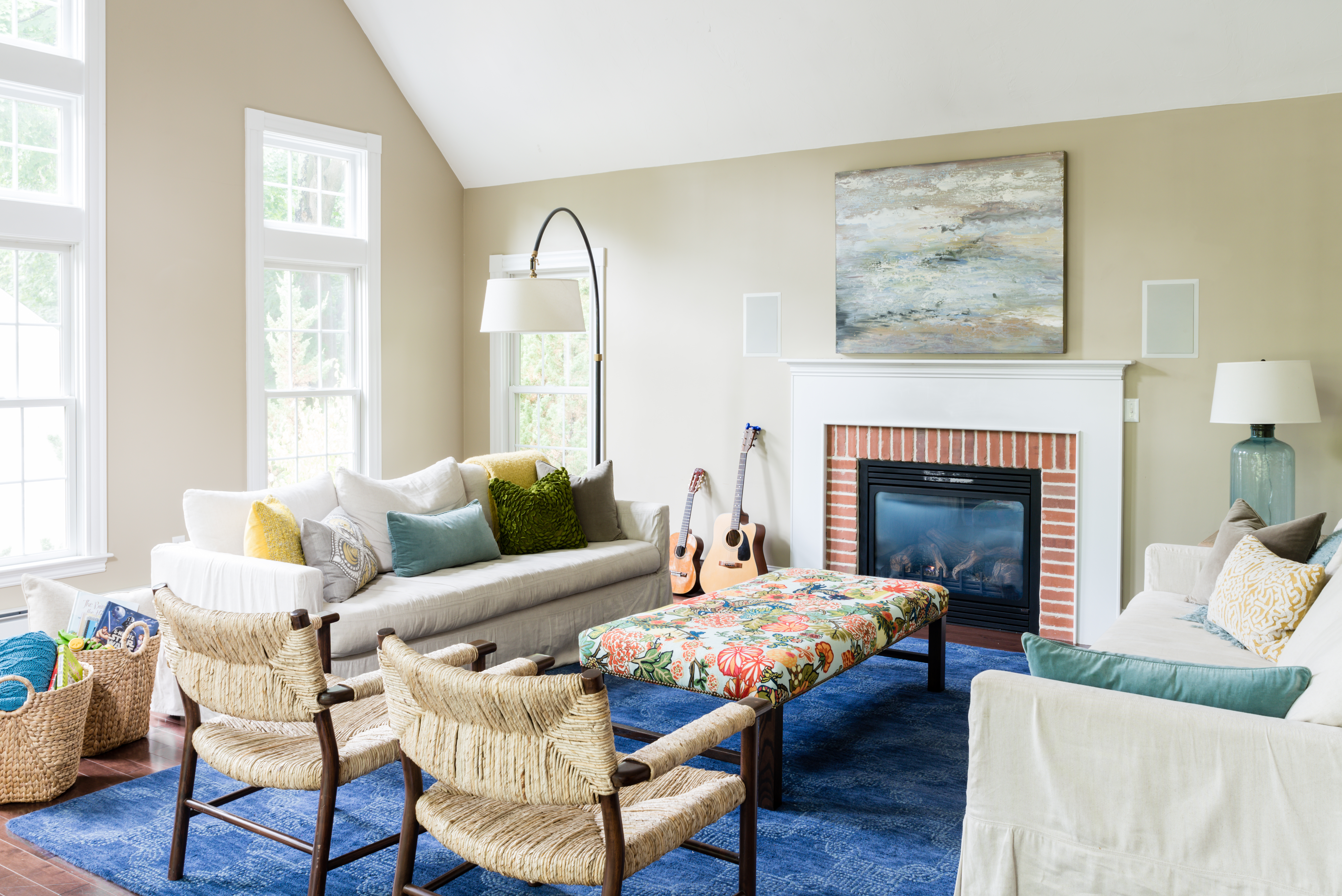 To liven up the neutral living room, designer Beth Bourque introduced a navy blue rug and a bench upholstered with a vibrant Schumacher fabric. On the linen slipcovered sofas, throw pillows in a mix of hues draw the eye and add textural interest.