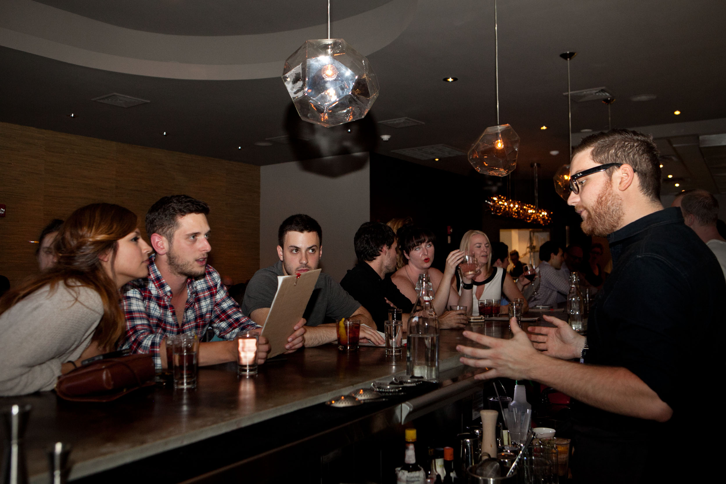 Brookline, MA -- 08/15/13 -- Bartender Philip MacLeod speaks with customers Karina Celis(left) and Max Ferullo(middle, in plaid) about cocktails at the bar at Ribelle restaurant in Brookline, Massachusetts on August 15, 2013. (Kayana Szymczak for the Boston Globe) 25dining