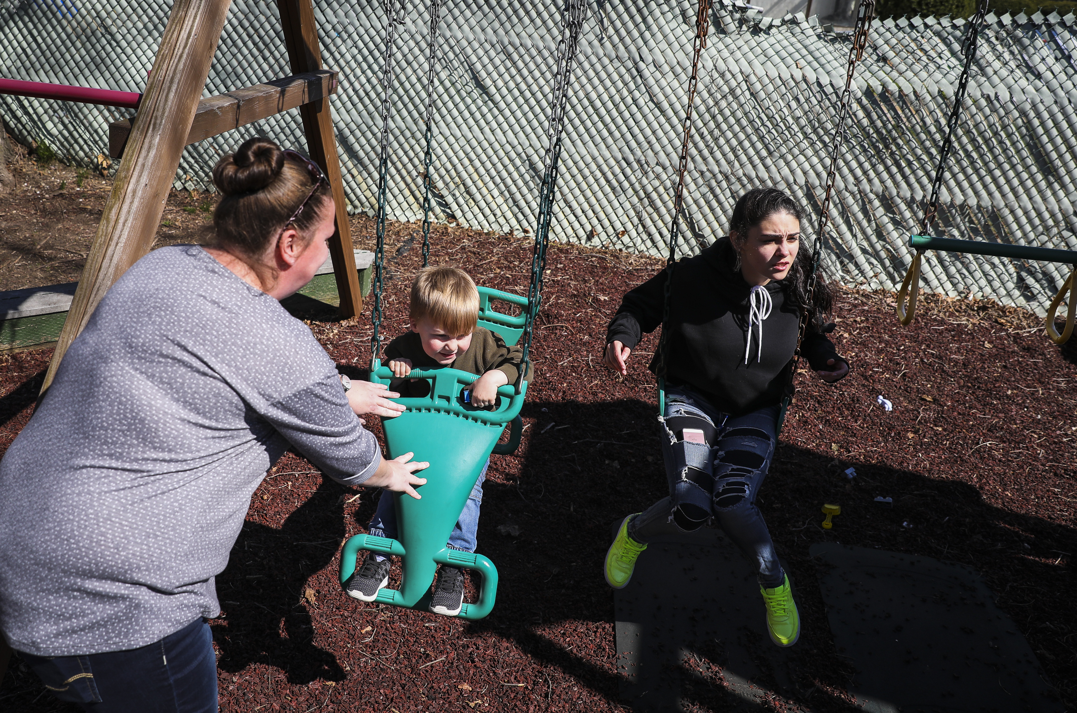 Erin pushed her 3-year-old son on the swing while they spent time outside with another shelter resident, Megan Toro (right) at the Family Life Education Center in Medford.
