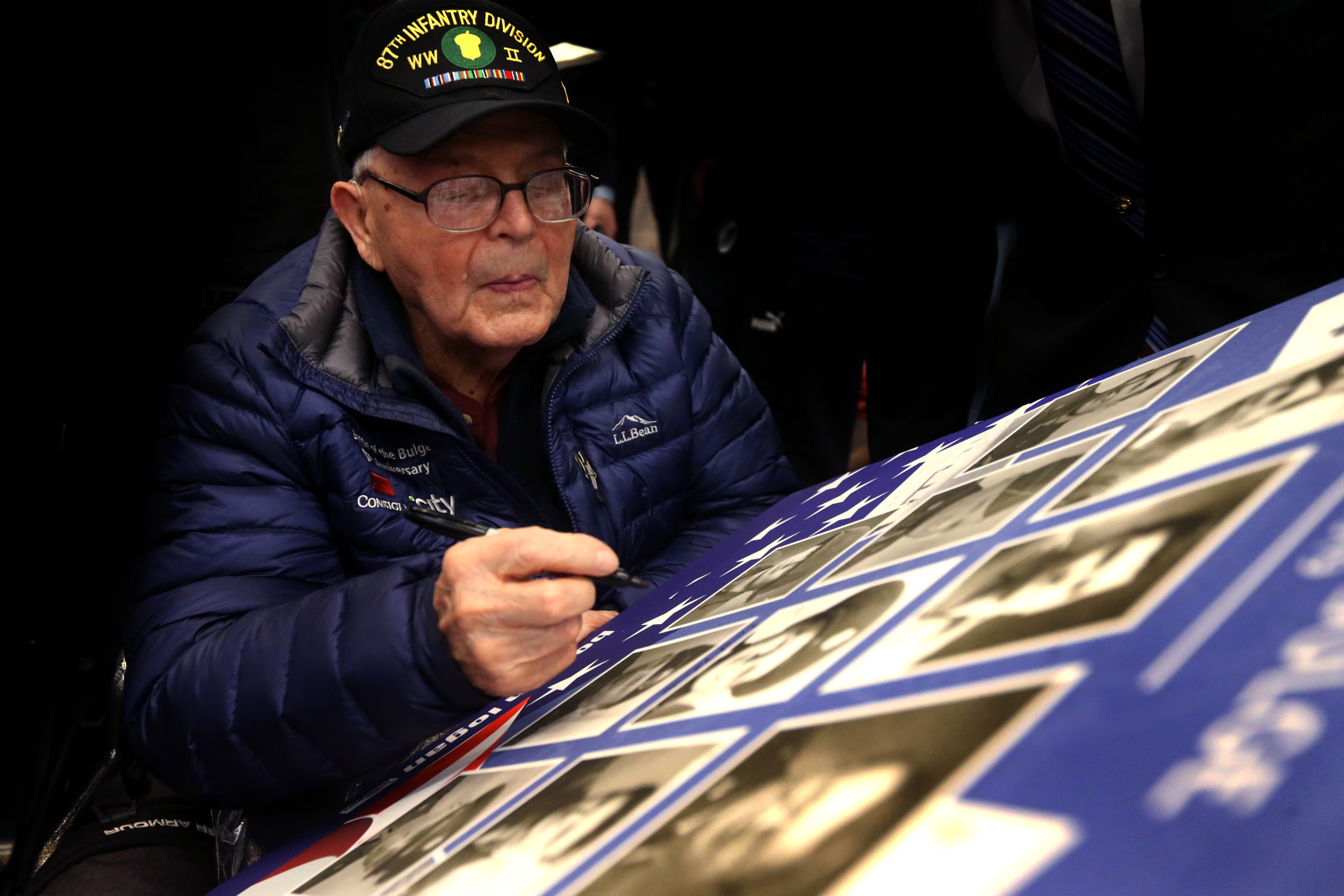 Ernie Roberts of Rhode Island signed a poster at Logan Airport before he departed for France to commemorate the 75th anniversary of the Battle of the Bulge.