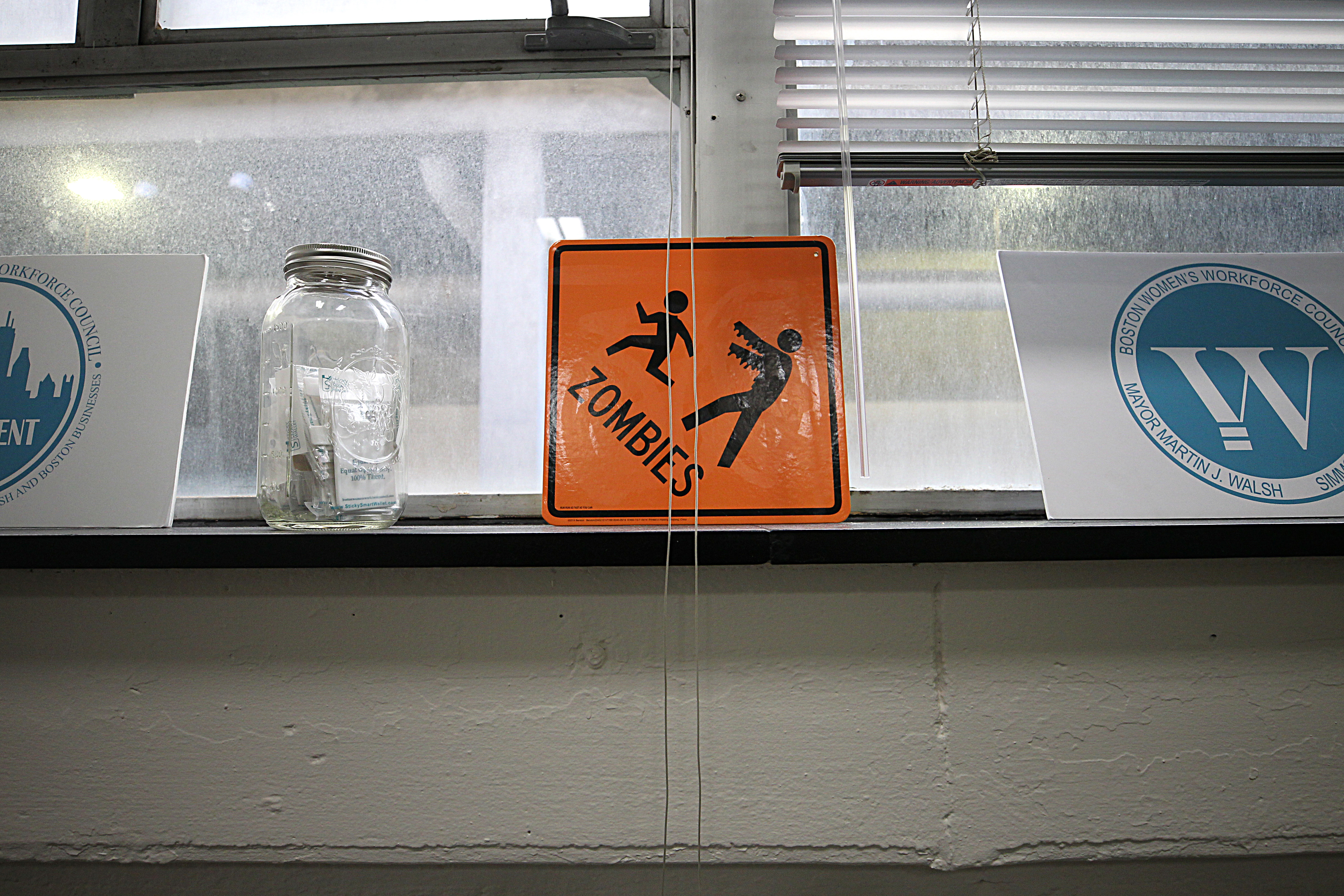 An orange construction-zone-like sign with the word “zombies” and a figure with outstretched arms chasing a smaller figure sits on the windowsill — left over from a Halloween party.