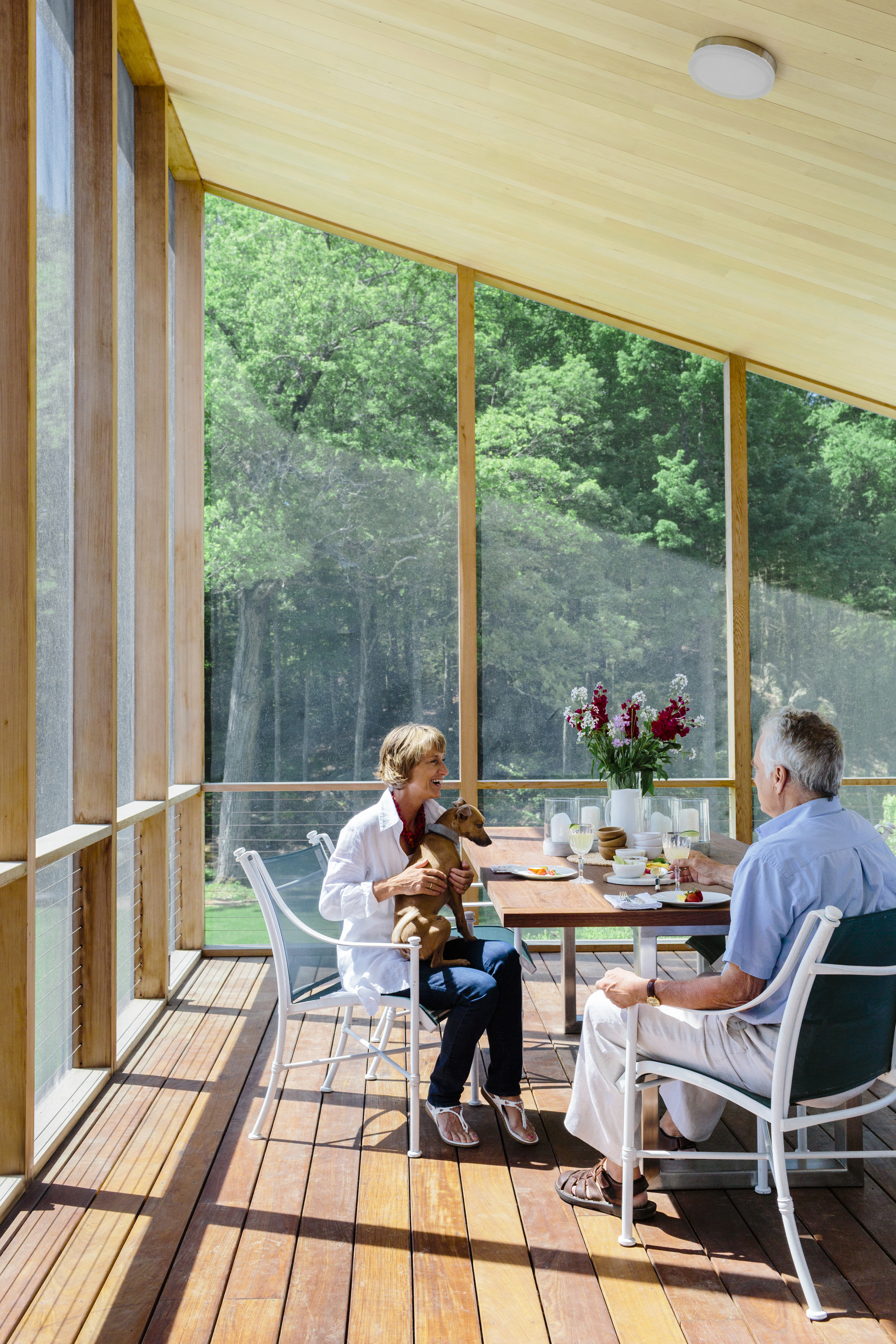 Eva and Fred Fierst relax on their screened dining porch, just a few feet from the kitchen’s food-prep area and built on a deck constructed of ultradurable ipe wood. A sleek custom table accommodates meals with the couple’s grown children and friends.