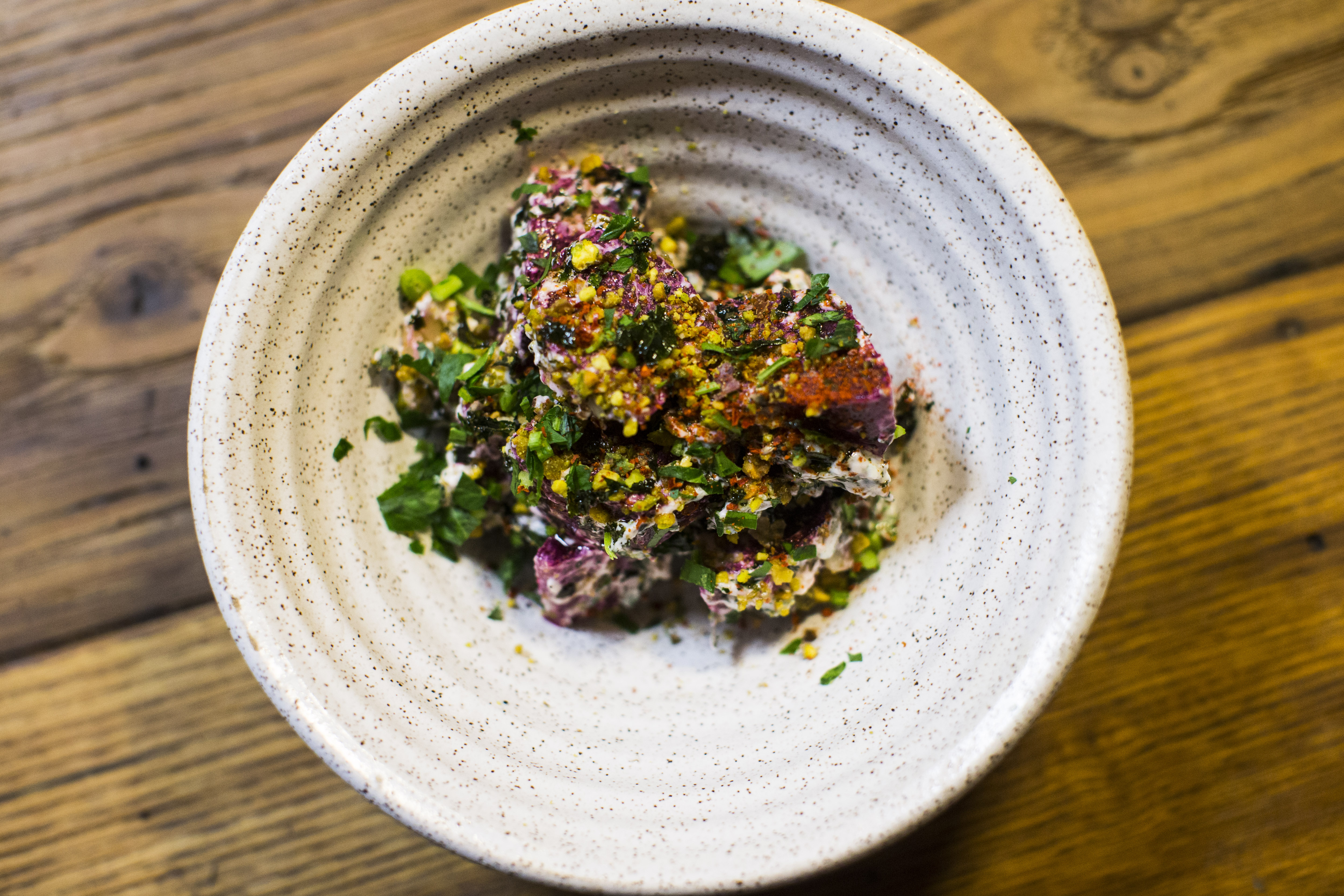 A bowl of beets with yogurt, pistachio, and roasted kale.