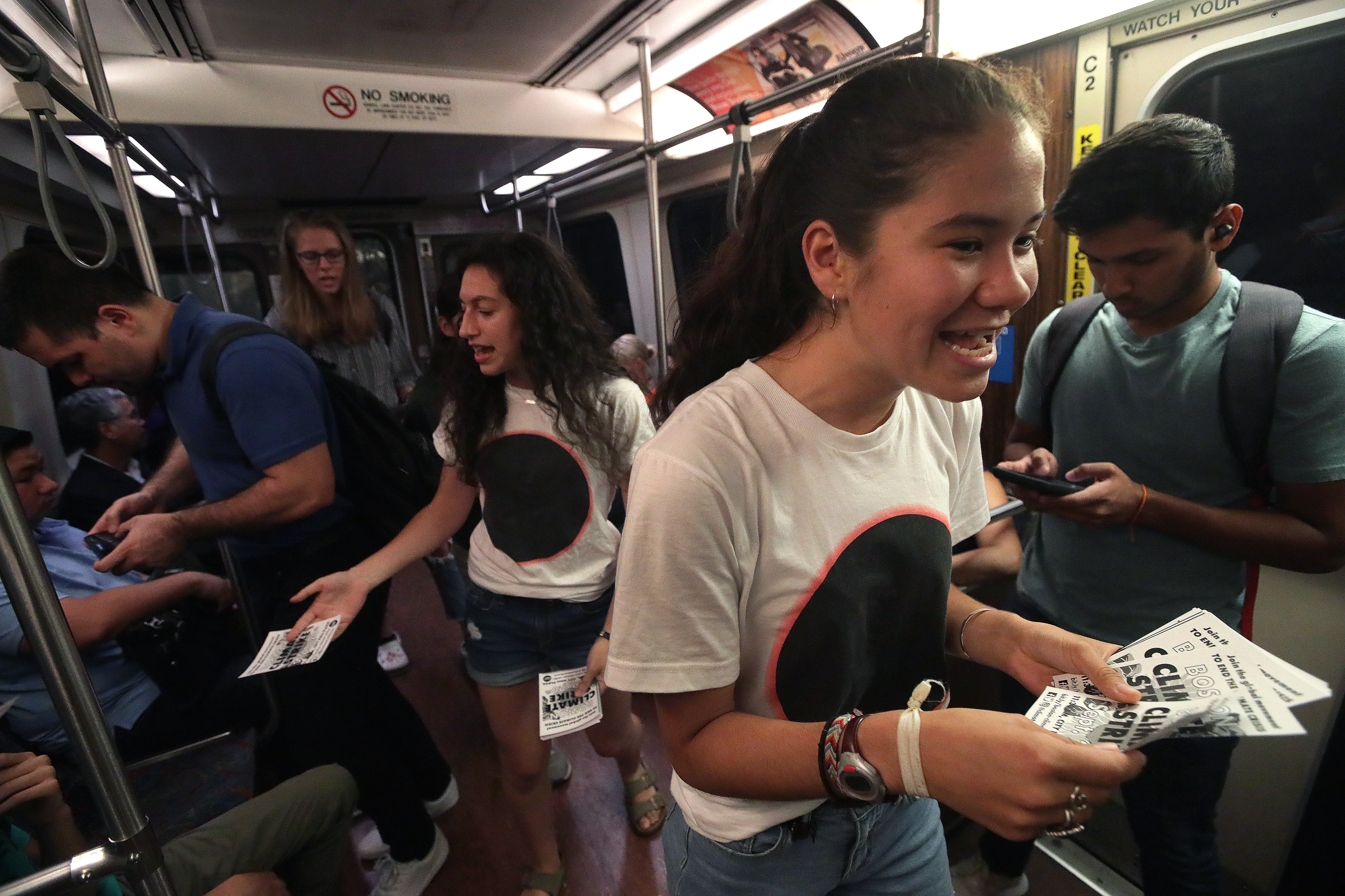 Emily Trelstad, 17, of Brookline (left), Amalia Hochman, 17, of Somerville, and Audrey Lin, 18, of Watertown pass out fliers on a rush hour train to inform the public of the Sept. 20 youth climate strike in Boston.