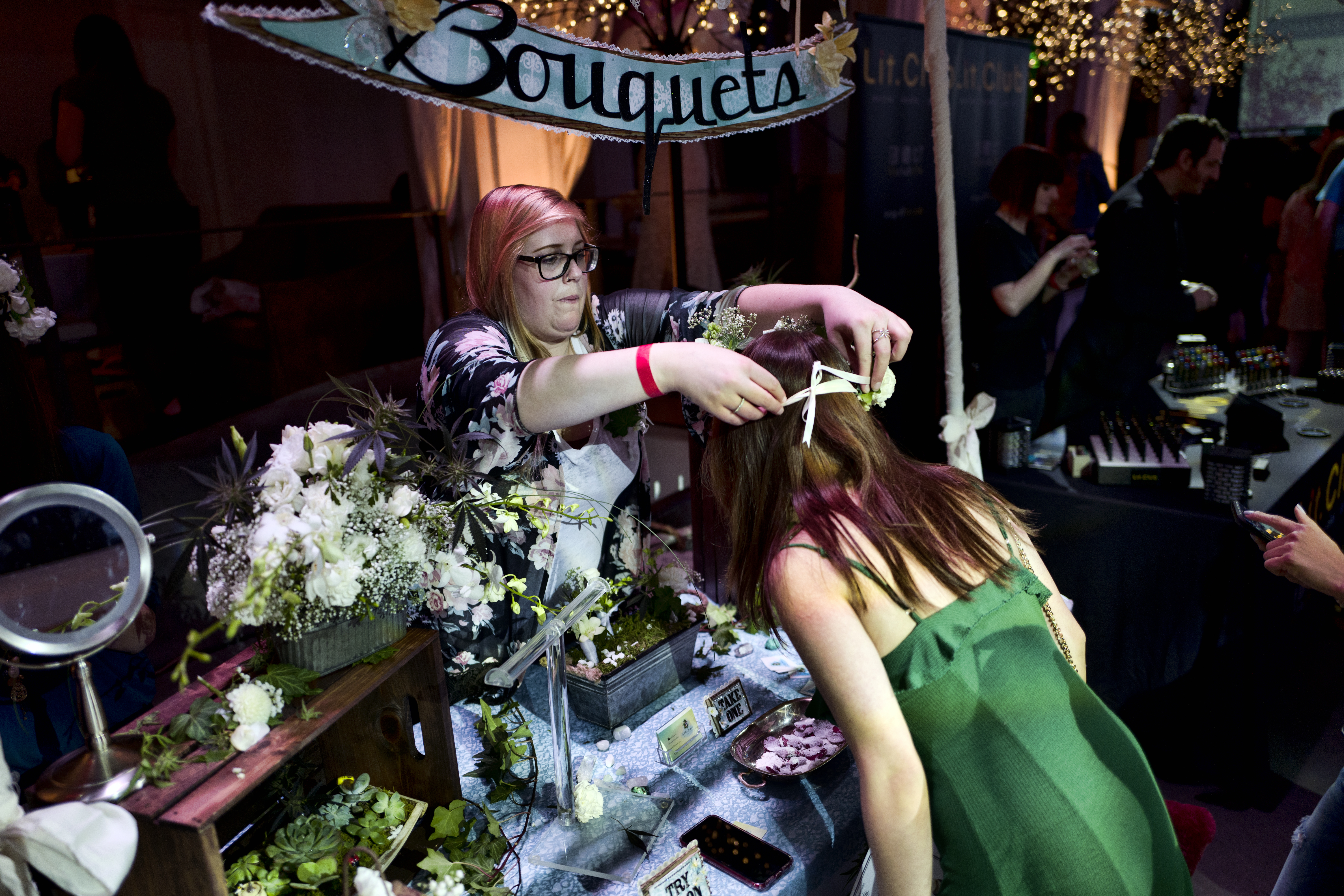 Jordyn Switzer with Bitchin' Bouquets, a floral service for all occasions, helps a visitor try on a floral headband using cannabis flowers.
