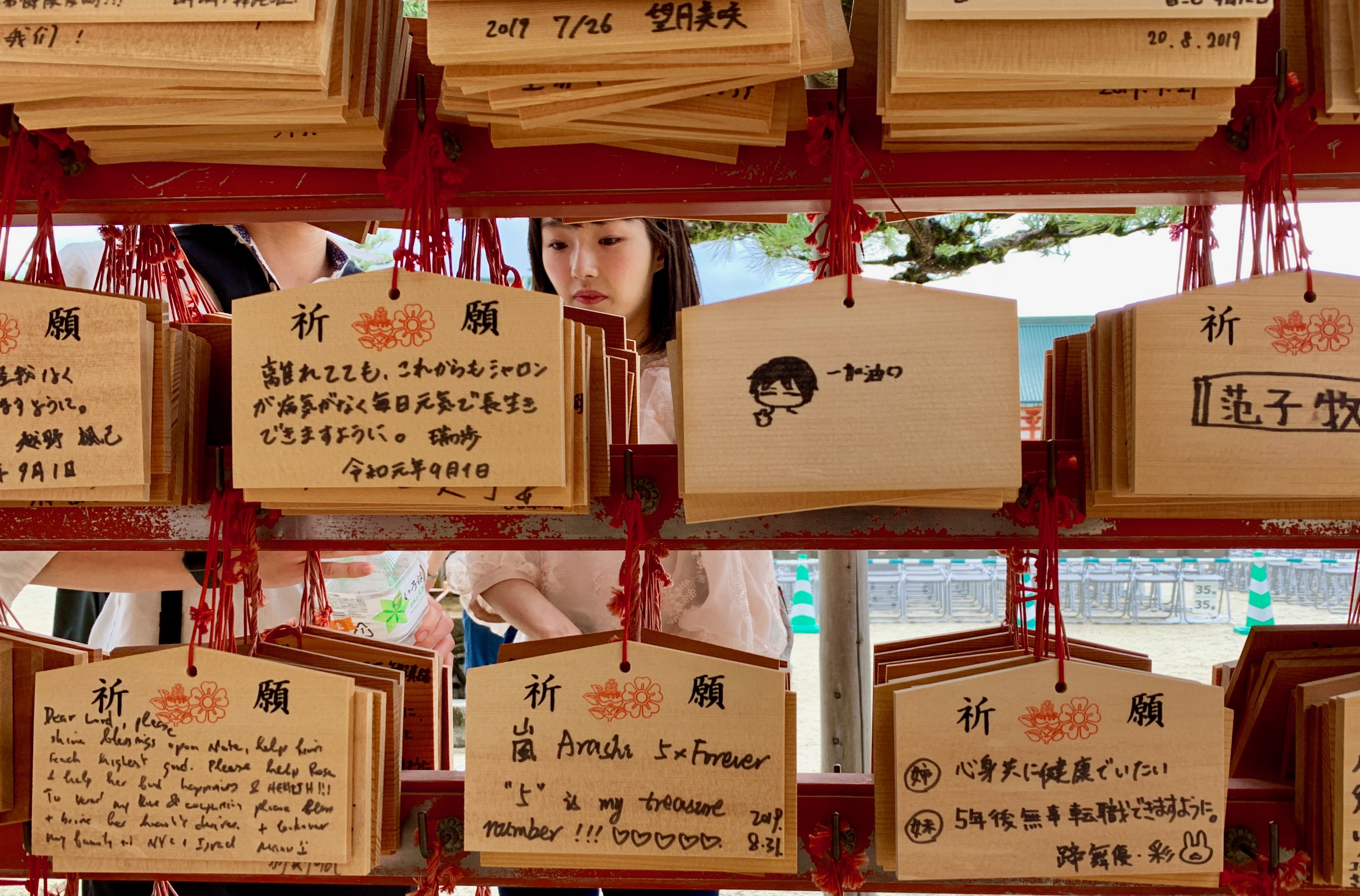 These Ema (votive tablets for writing wishes) are very popular in shrines around Japan. People write their wishes and leave the tablets hanging up at the shrine where the kami (Shinto deities) can receive them. A woman inspects the Ema at the Heian-Jingu shrine in Kyoto.