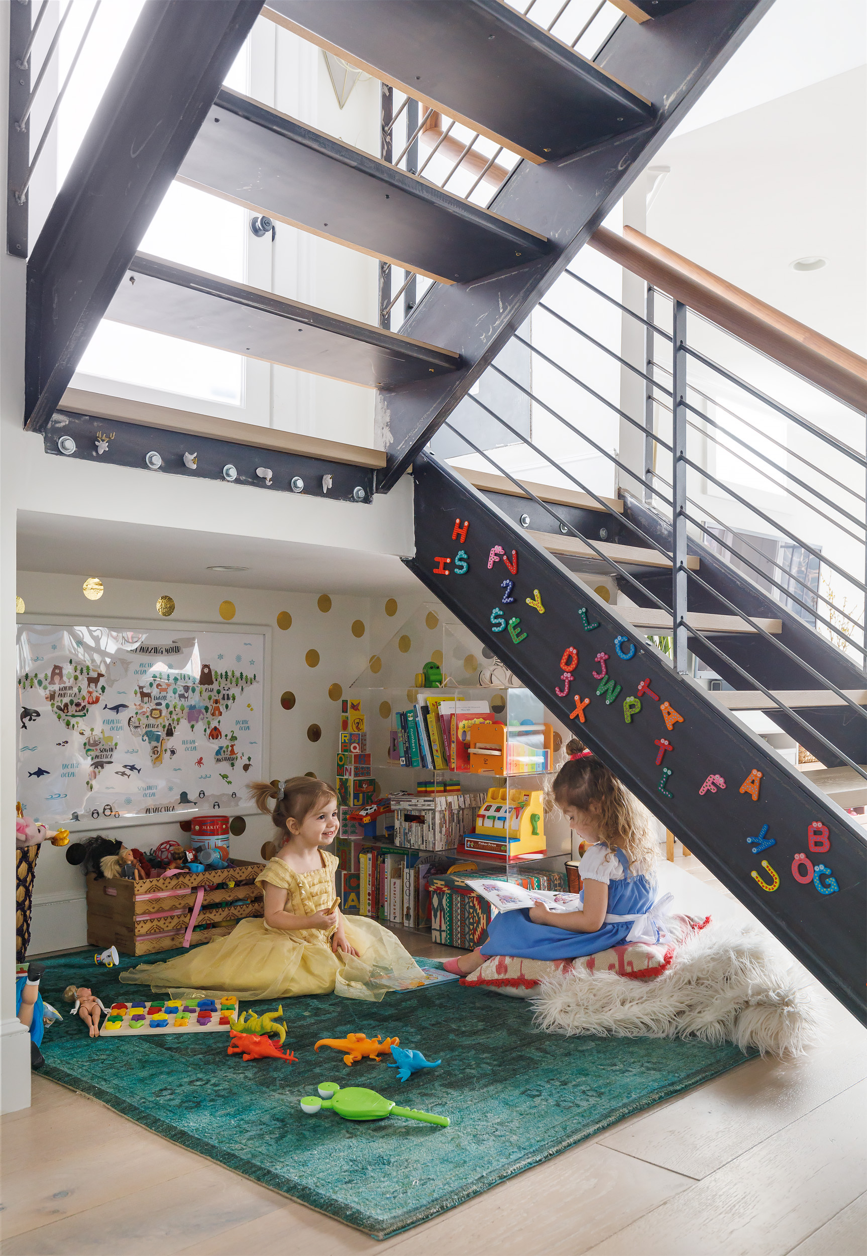 A former storage space under the stairs is now a play area outfitted with a house-shaped acrylic bookcase. The gold stickers are from Paper Source.