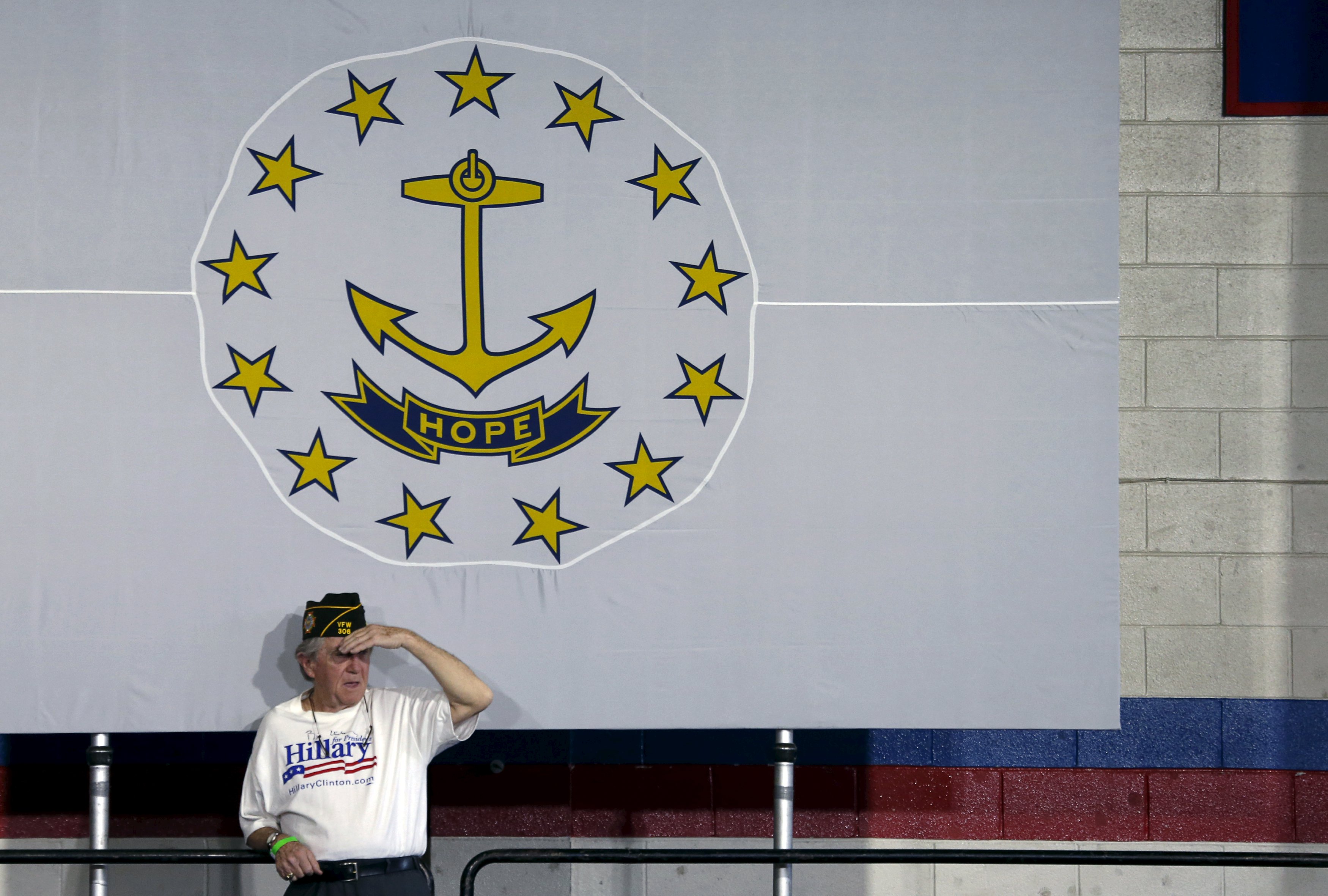 A veteran shielded his eyes as he stands on a back platform under a flag that reads “hope” before Hillary Clinton spoke during a campaign rally in Central Falls, Rhode Island on Saturday.