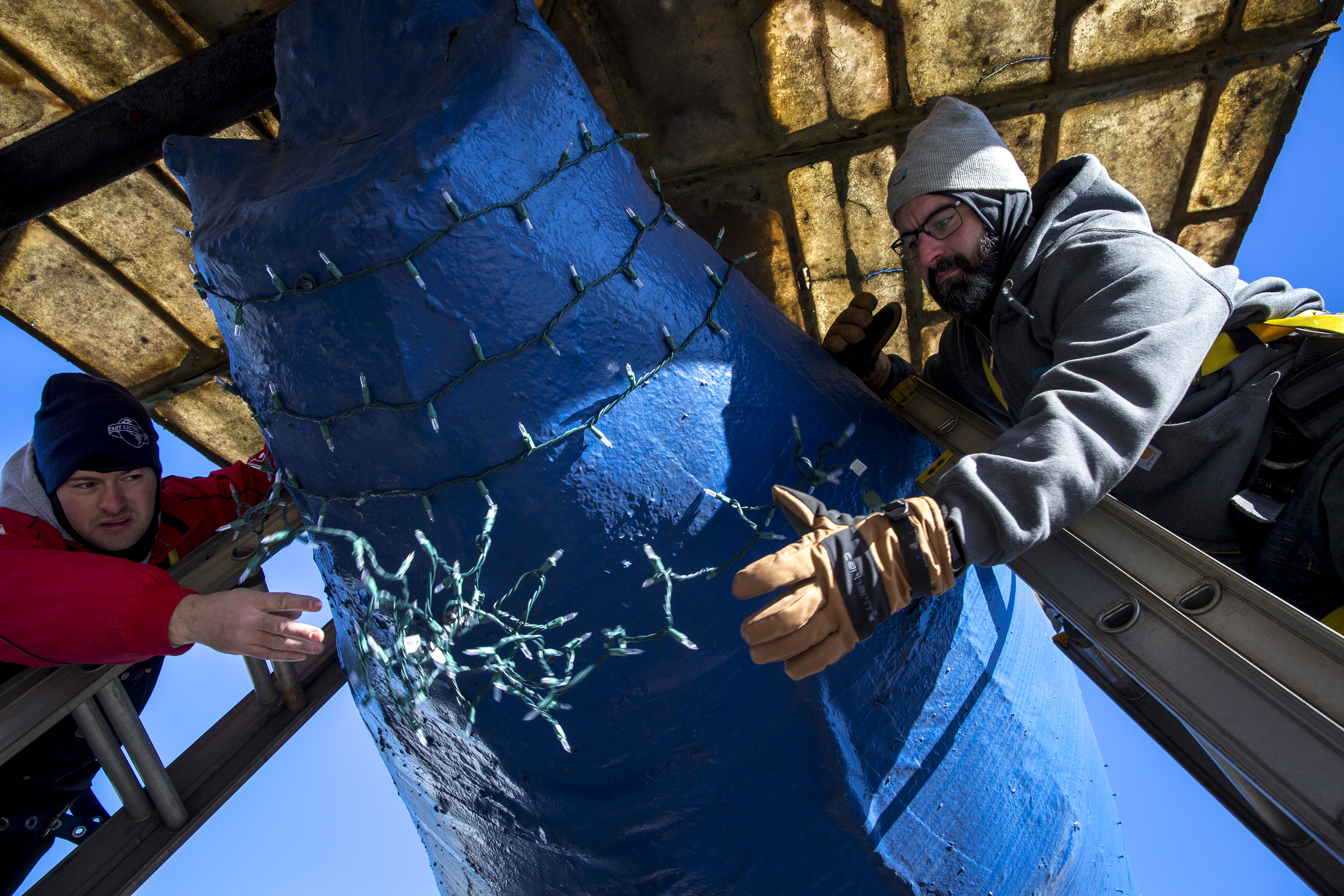 Giovanni Cippola (left) threw a string of lights to Anthony Lisi while decorating The Big Blue Bug.