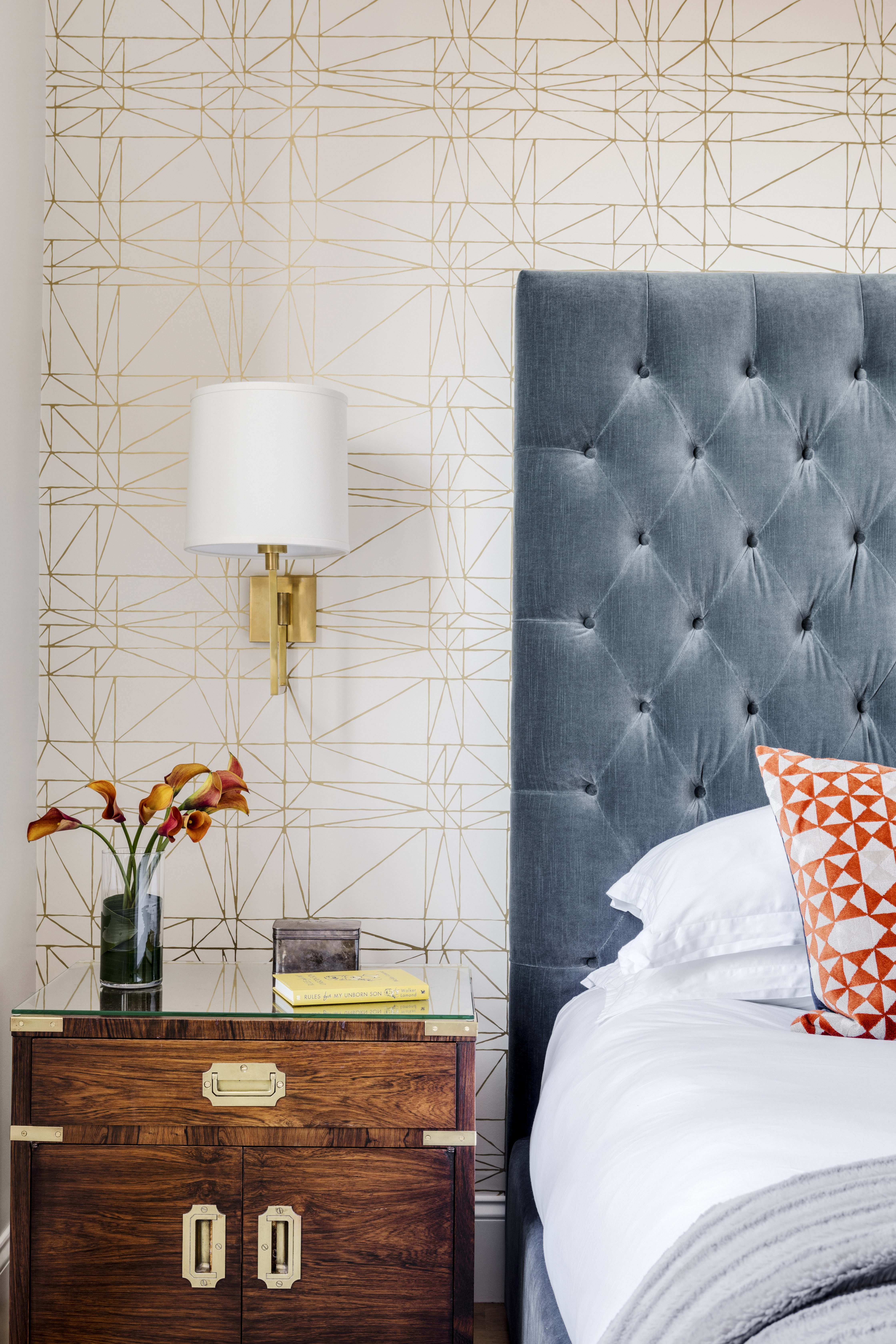 The tufted headboard of the Restoration Hardware platform bed is upholstered in slate blue velvet. Caroline chose the gold metallic geometric patterned Hygge & West wallpaper. The vintage John Stuart campaign-style nightstand is one of a pair Andrew already owned, bought online from InCollect.