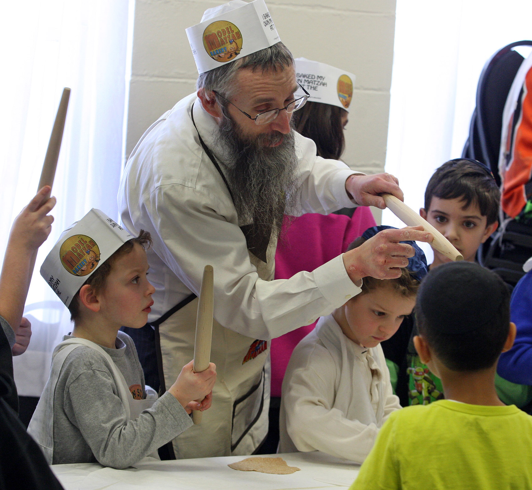 Rabbi Mendel Gurkow teaches students at Shaloh House Chabad in Stoughton how to make matzo, demonstrating rolling pins must be re-sanded after use.