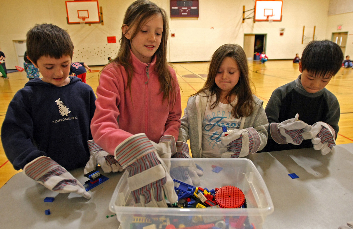 Sharon third-graders (from left) PJ McManus, Eva Wallace, Amelia Scappaticci, and Allen Zhang try their hand at a dexterity activity with Lego bricks while wearing “space gloves.’’