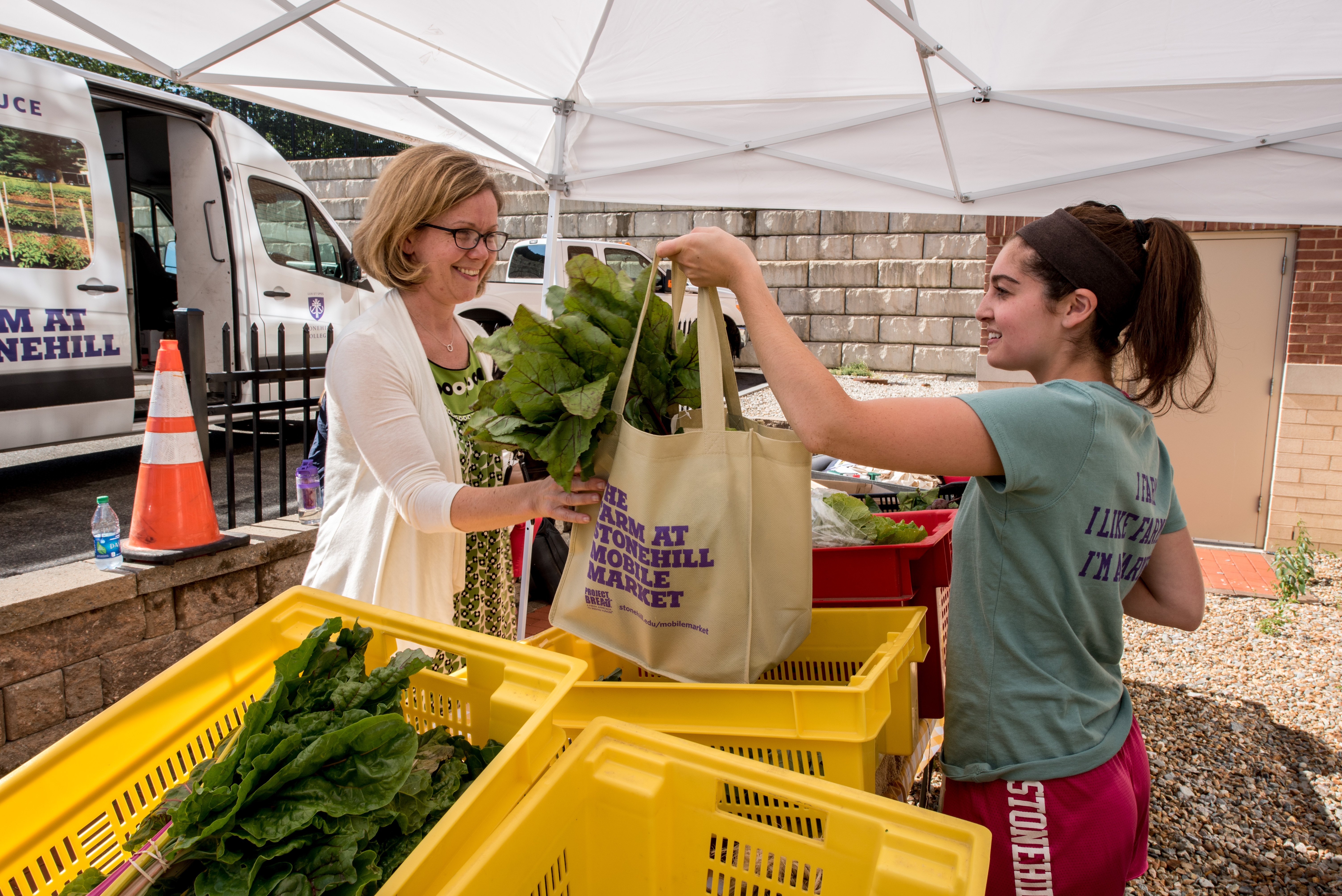 Alexandra Avedisian (left) of Brockton Neighborhood Health Center buys produce from Melissa Mardo, a Stonehill College student and an intern at its Mobile Market.