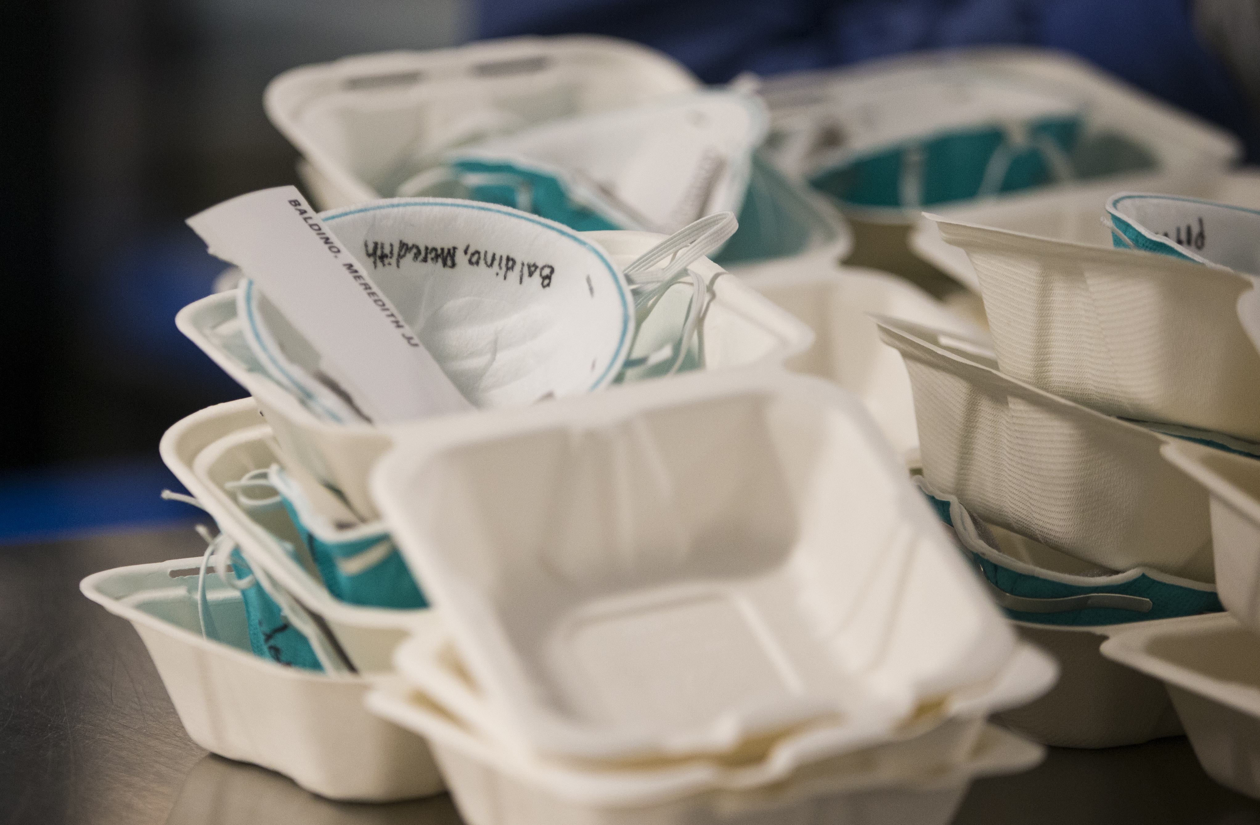 Piles of N95 masks, each with a label and name wait to be sorted.
