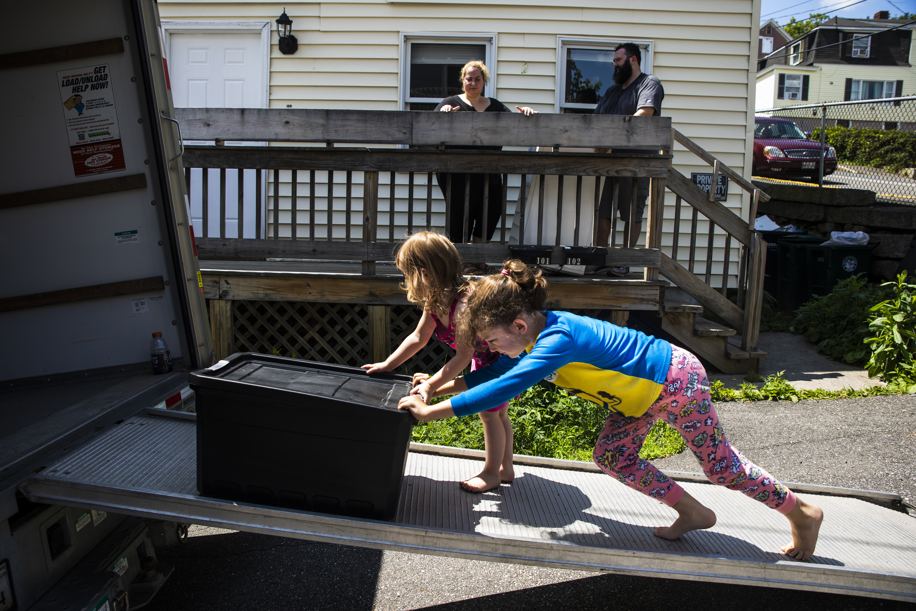 Laya (left) and Evan pushed a tote up the ramp of the U-Haul while their parents, Mariah LeMieux-Lupien and Patrick Lupien, watched from the porch of their apartment. “More, more, more!” yelled Laya, after stacking the tote in the back of the truck.