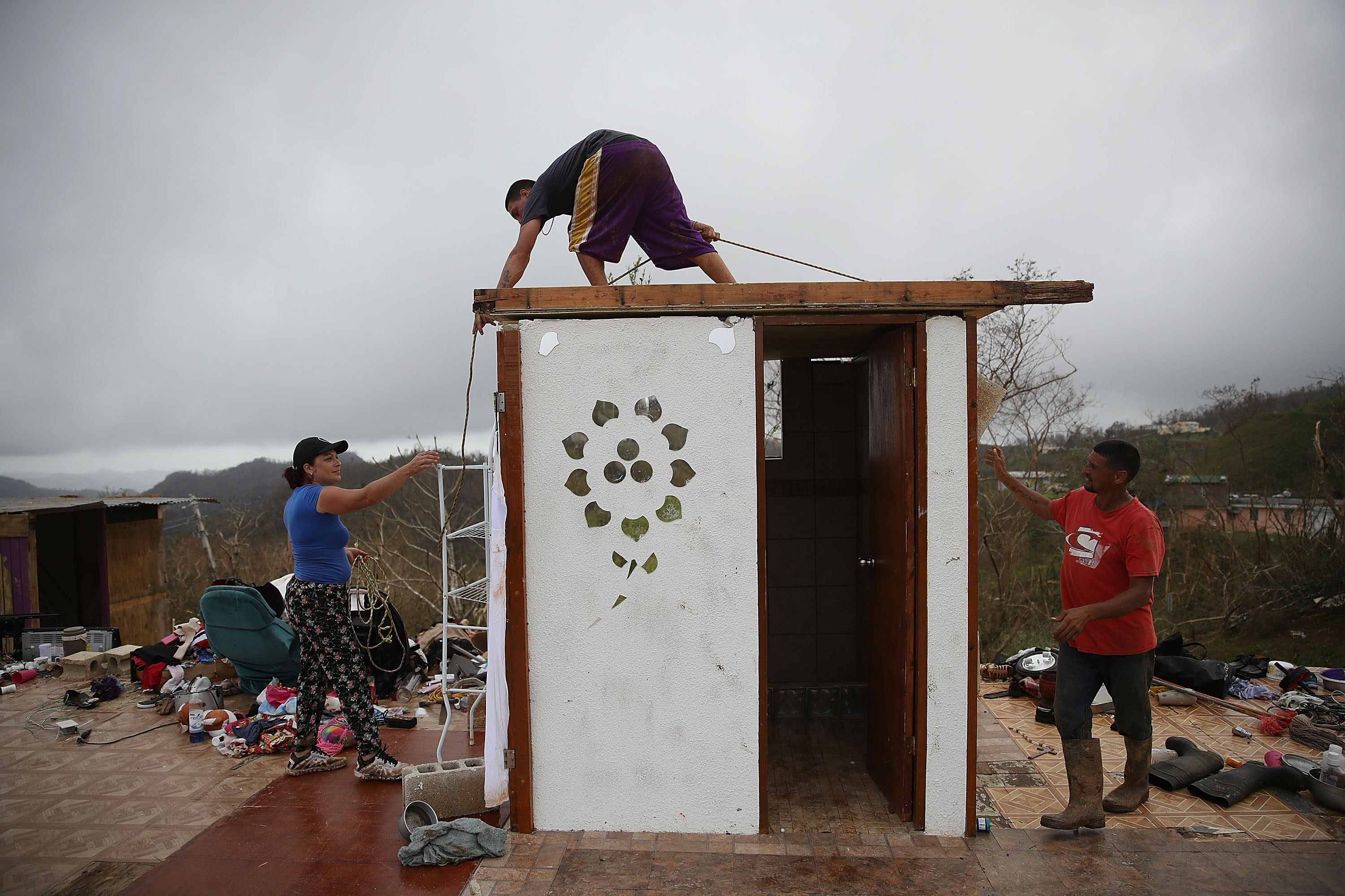 Carmen Maldonado, Jose Flores and Carlos Flores (left to right) put a temporary roof the bathroom which is all that is left of their home.
