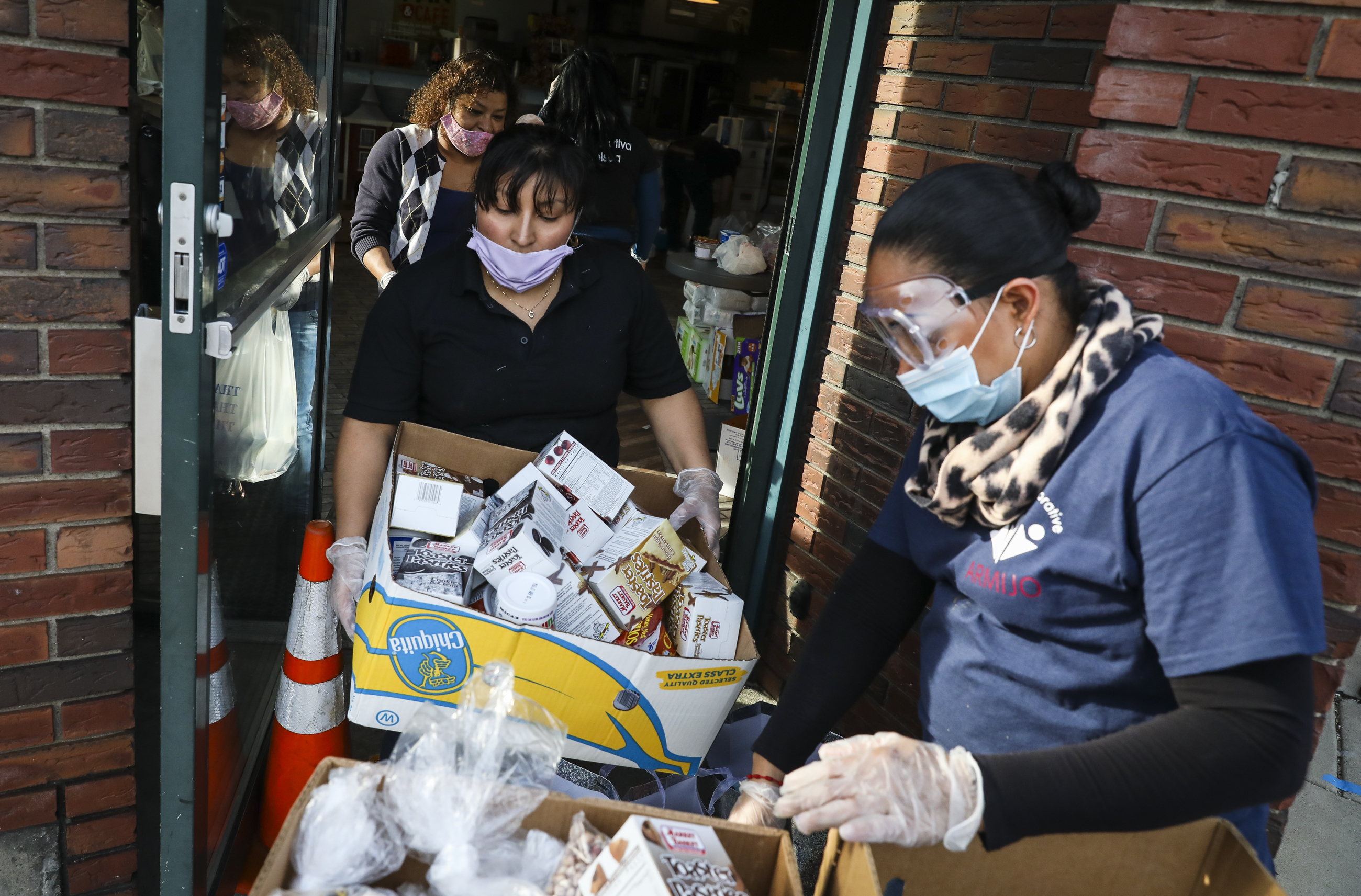 Gladys Socop, left, brought out a box of groceries to Jessica Armijo while volunteering in a pop-up food pantry hosted by Pan Y Cafe. Organized by Chelsea Collaborative, the food distribution has been operating for over 3 weeks with food donated by local businesses and food pantries and delivered to at-need families in Chelsea.