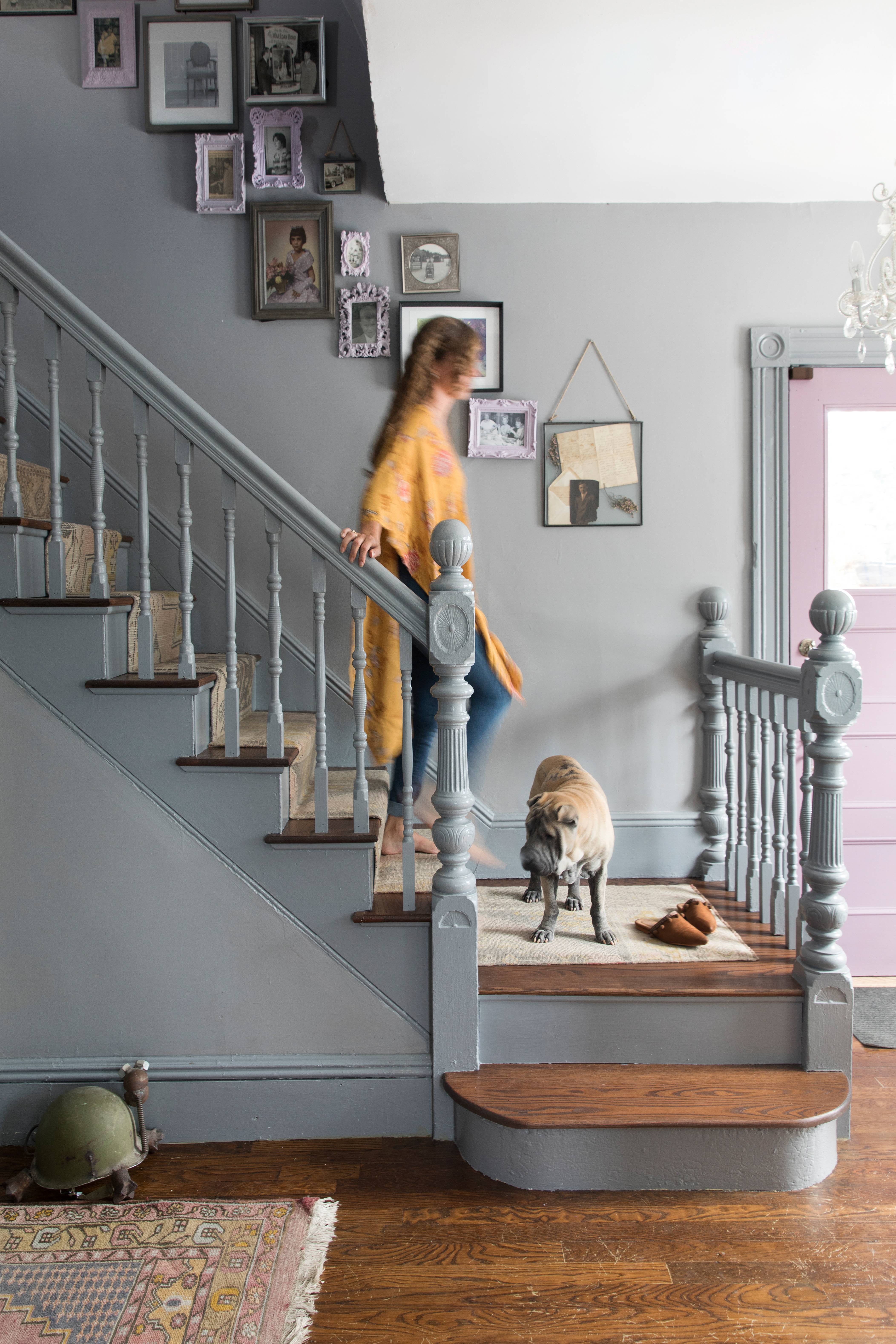 Dewhirst and Moose on the stairs. The family photos are in HomeGoods frames she painted lavender. “I’m the family historian,” she says.