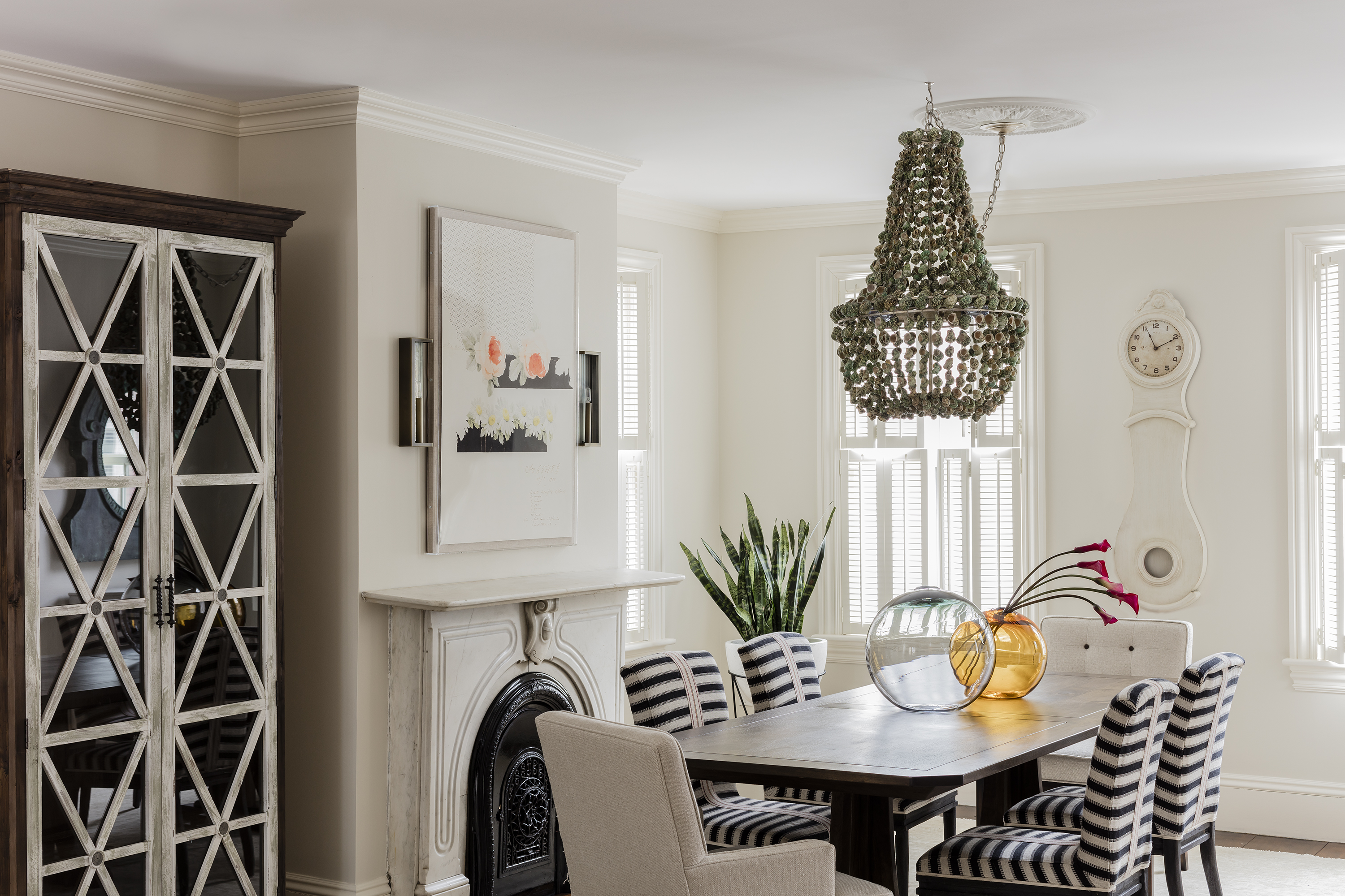 Nineteenth-century touches, like a marble fireplace and ceiling medallions, juxtapose with modern furnishings, including a seashell chandelier and boldly striped chairs.