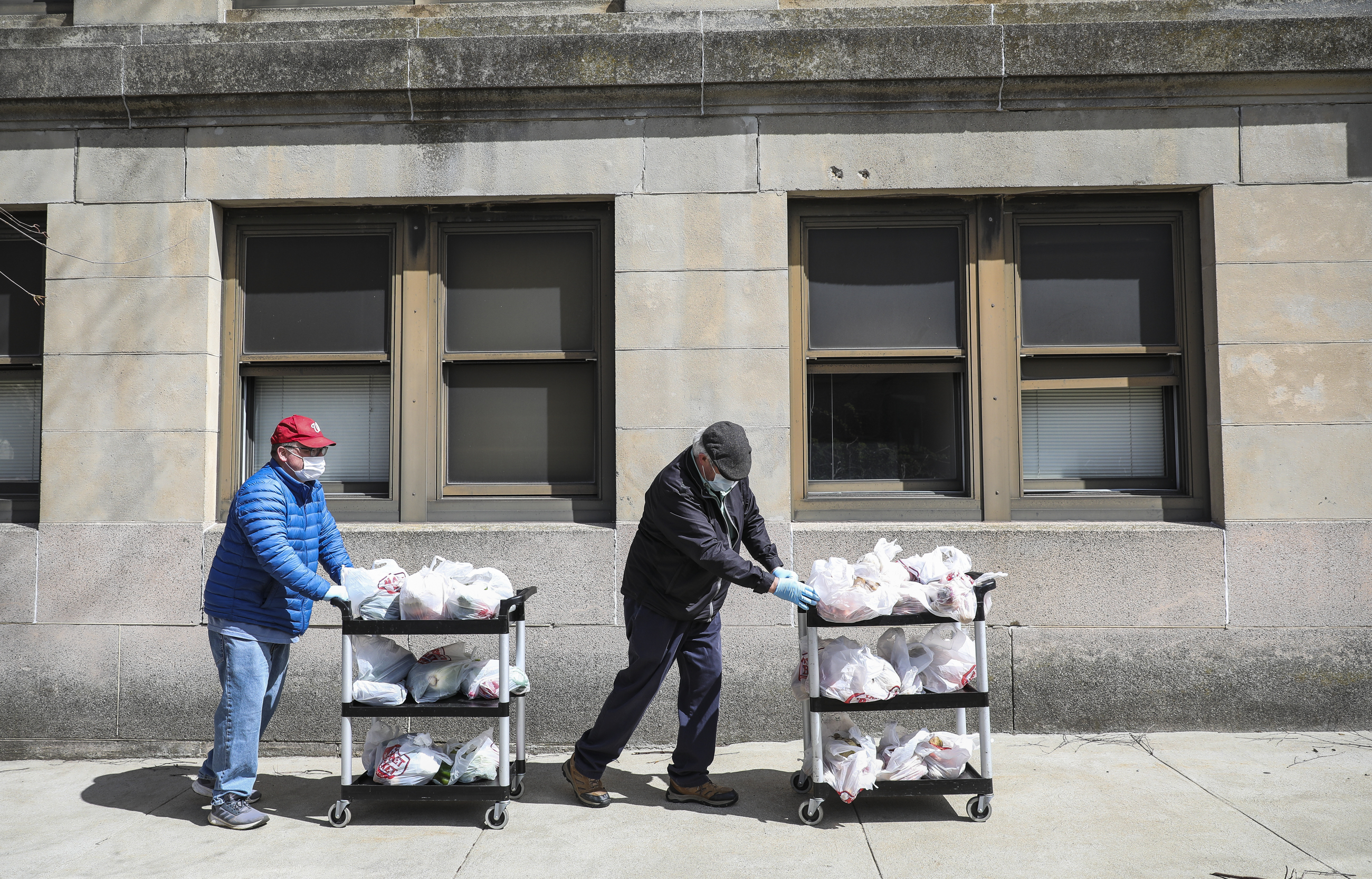 Waltham city councilor-at-large Pat O'Brian (left) and Waltham city councilor John McLaughlin pushcarts full of vegetables and fruits to be given away to Waltham residents.