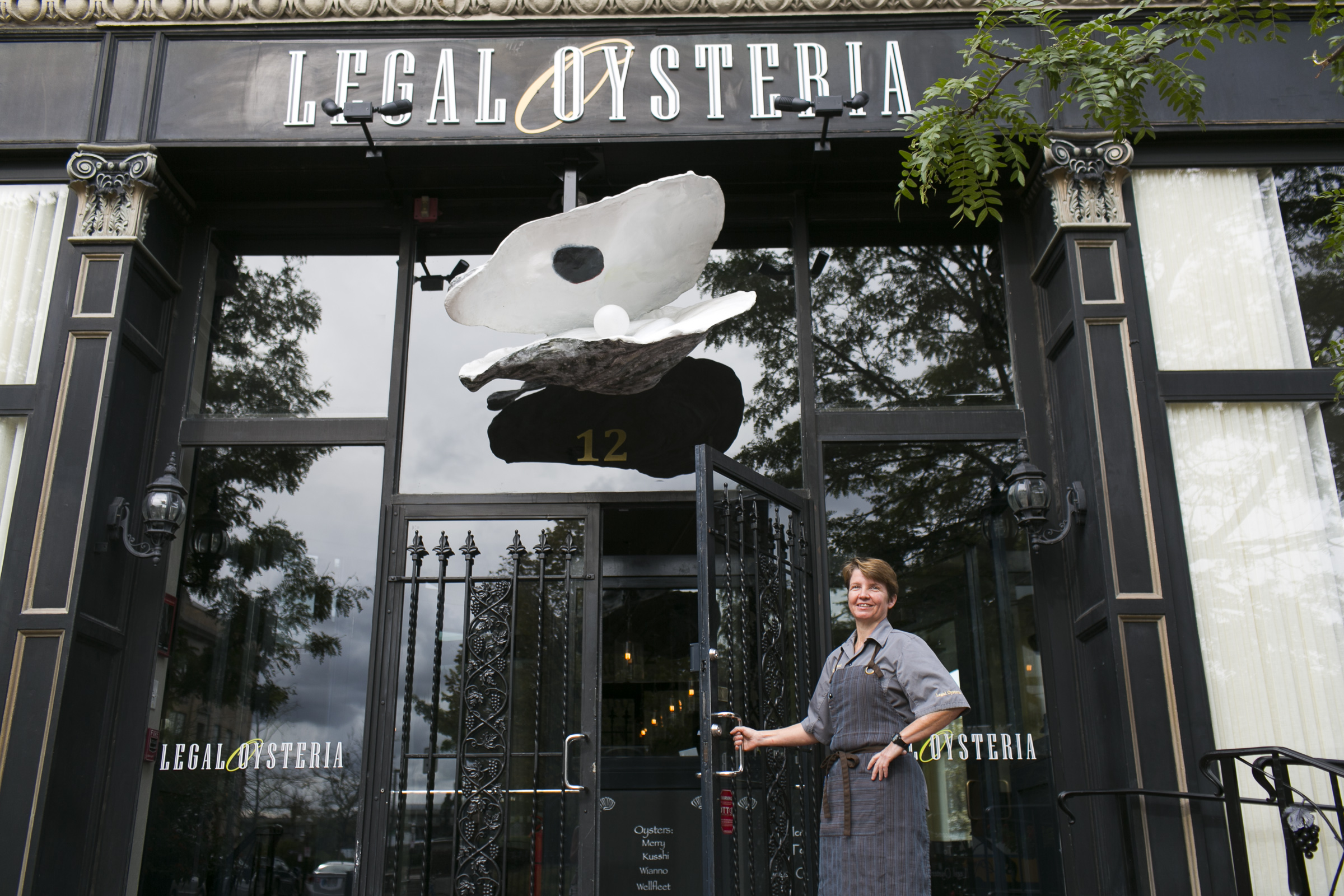 Chef Gina Palmacci stands at the doorway to Legal Oysteria in Charlestown. A large oyster with a “pearl” in it adorns the entrance.