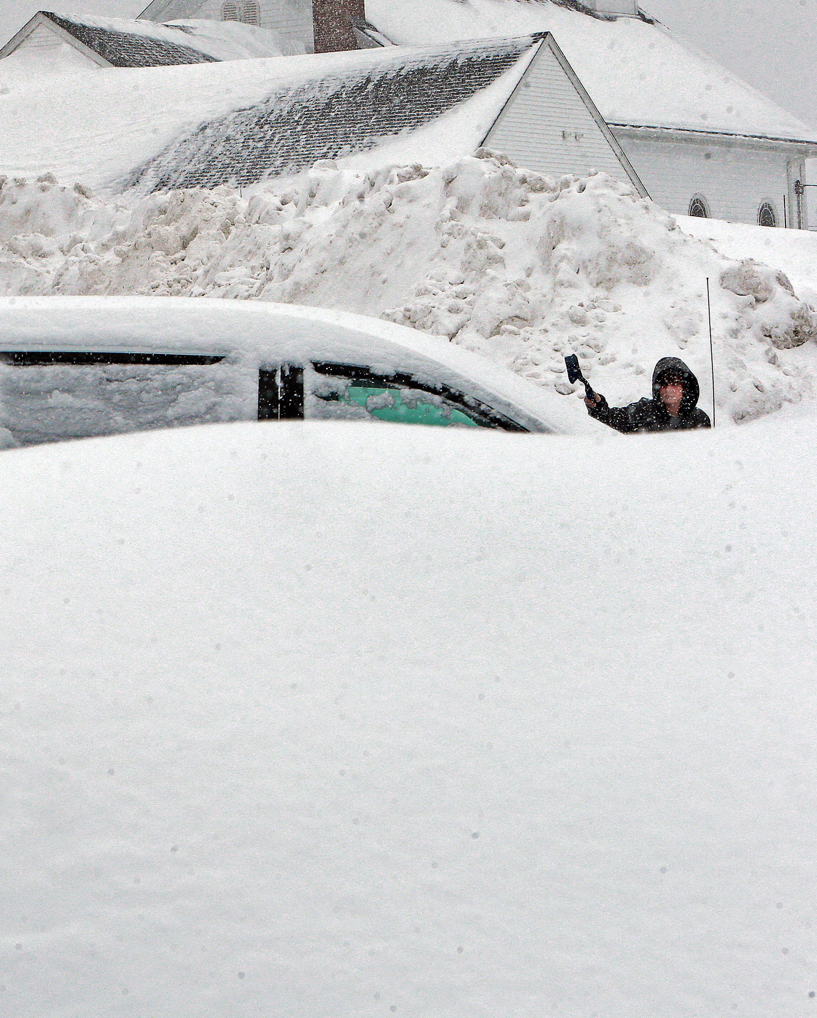 Ryan Burke of Lynn cleared a car of snow in a parking lot behind St. Michael Church in North Andover on Monday. The pile behind him was amassed during earlier storms.