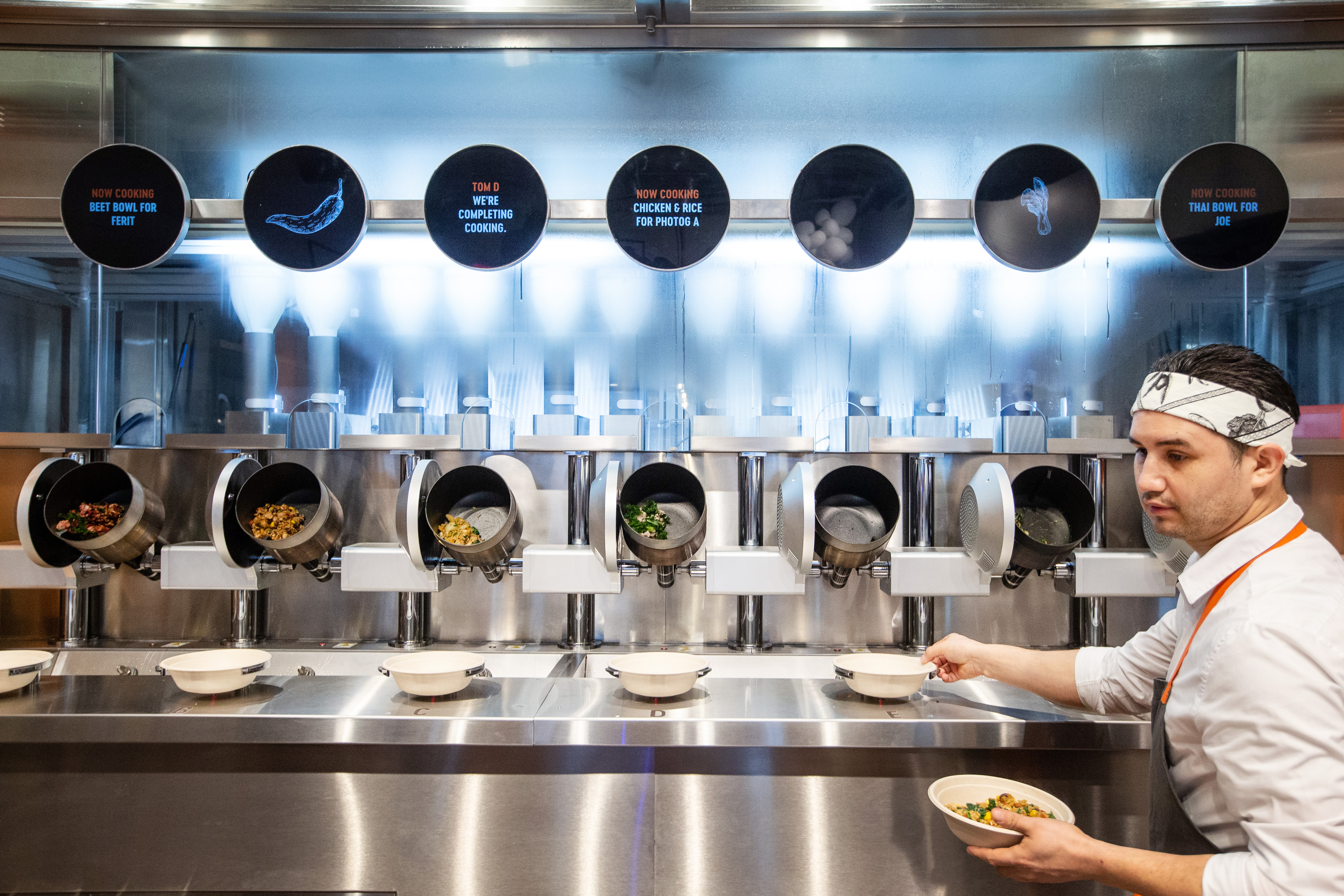 A robot uses displays to show what it is cooking and for who at Spyce in Boston.