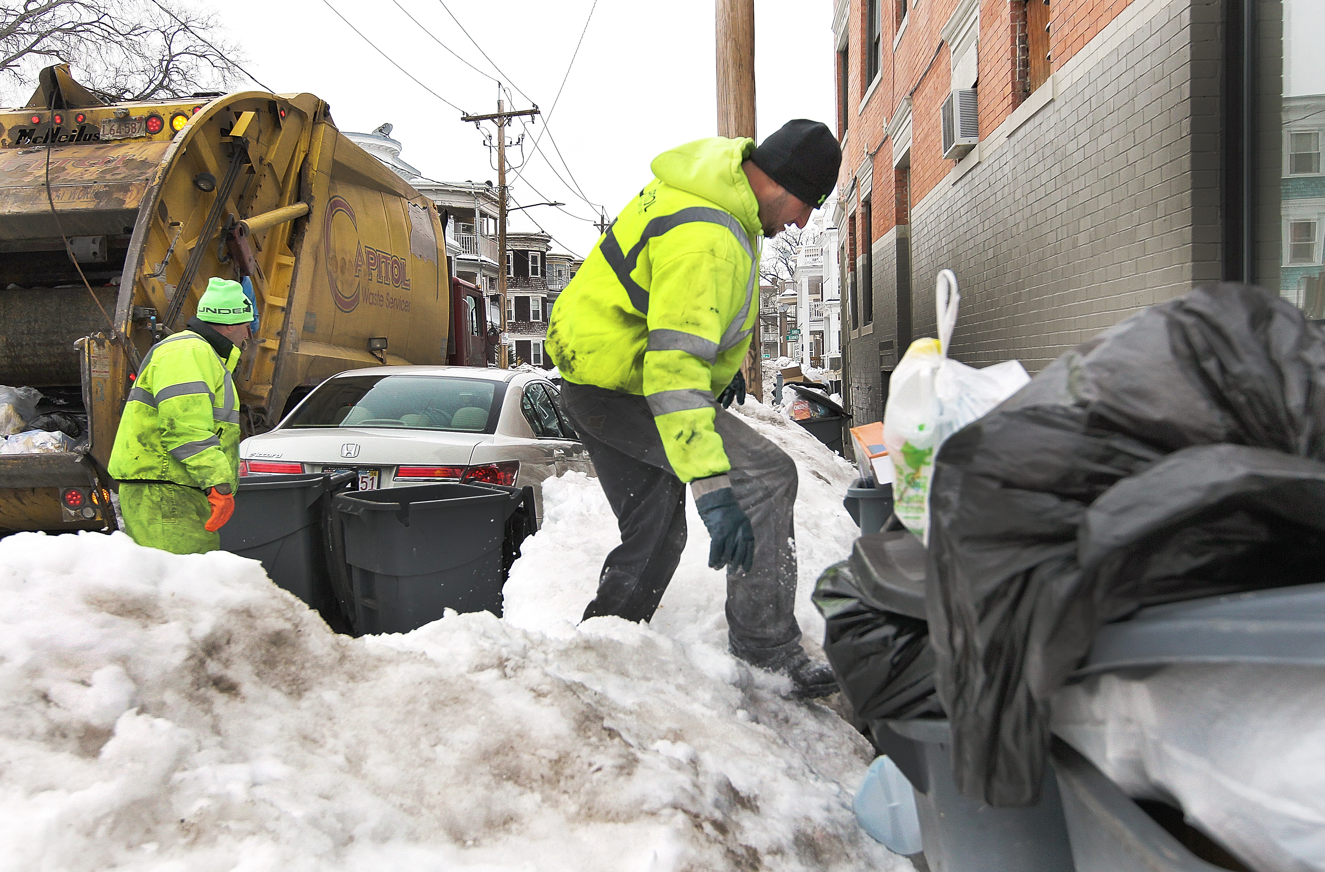 Capital Waste Services employee Jose Andrade climbed a snowbank to pick up bags of garbage on Sumner Street in Dorchester on Thursday.