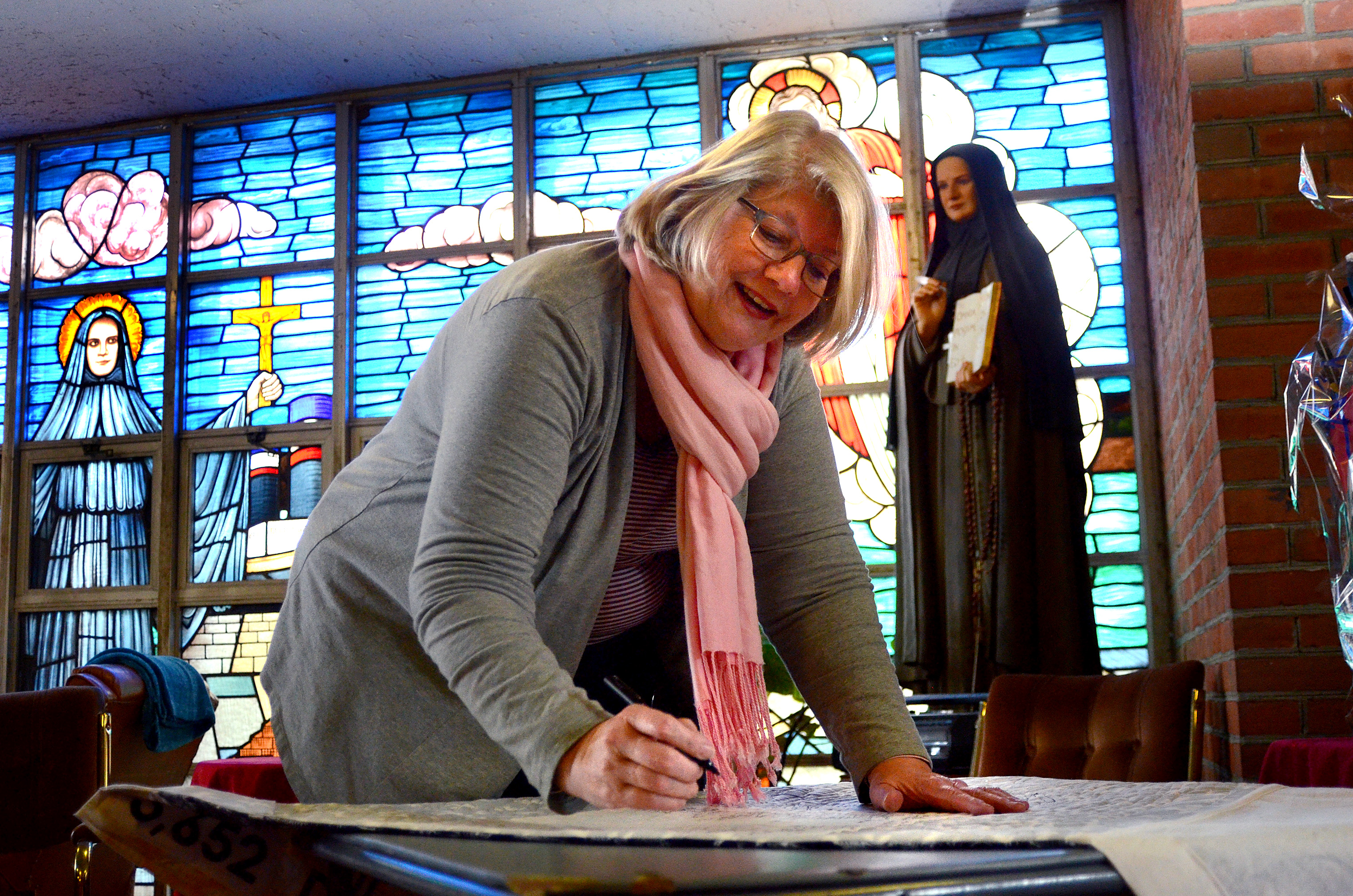 Parishioner Peg O'Brien signs the 10th anniversary quilt.