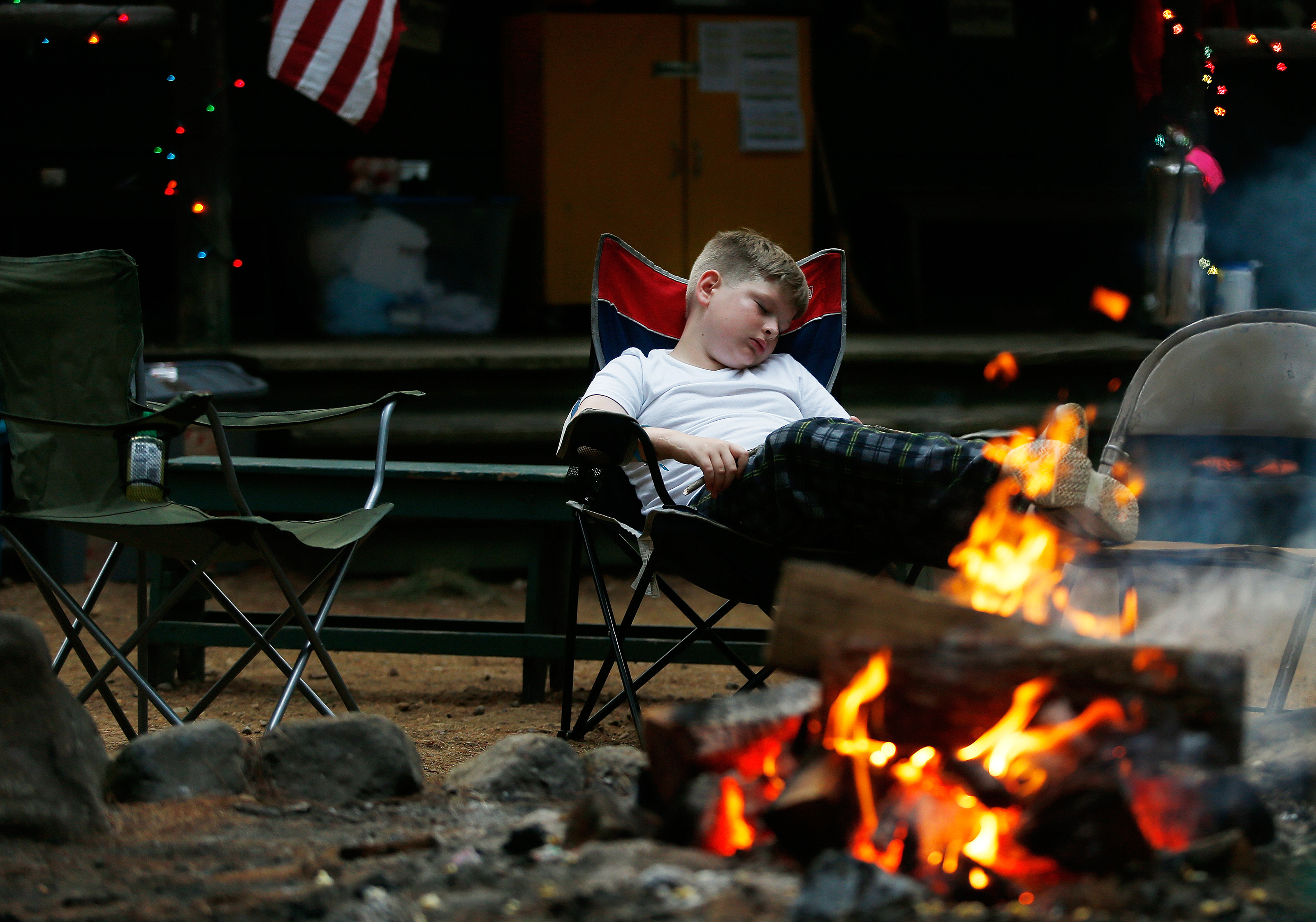 A camper relaxed near the wood fire.