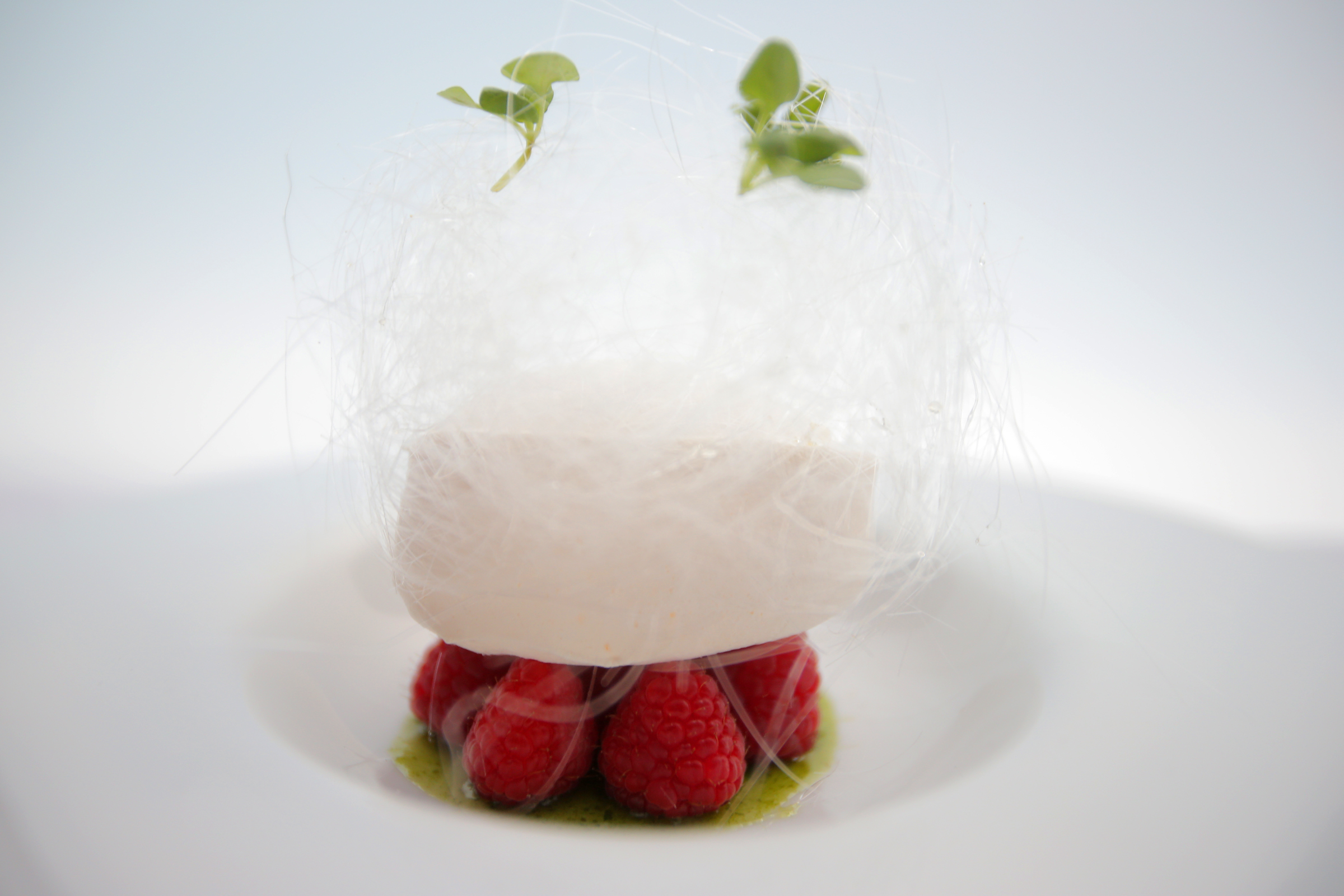 A “snow egg” features a pillow of meringue atop raspberries with lemon curd mousse, basil syrup, and a crown of spun sugar.