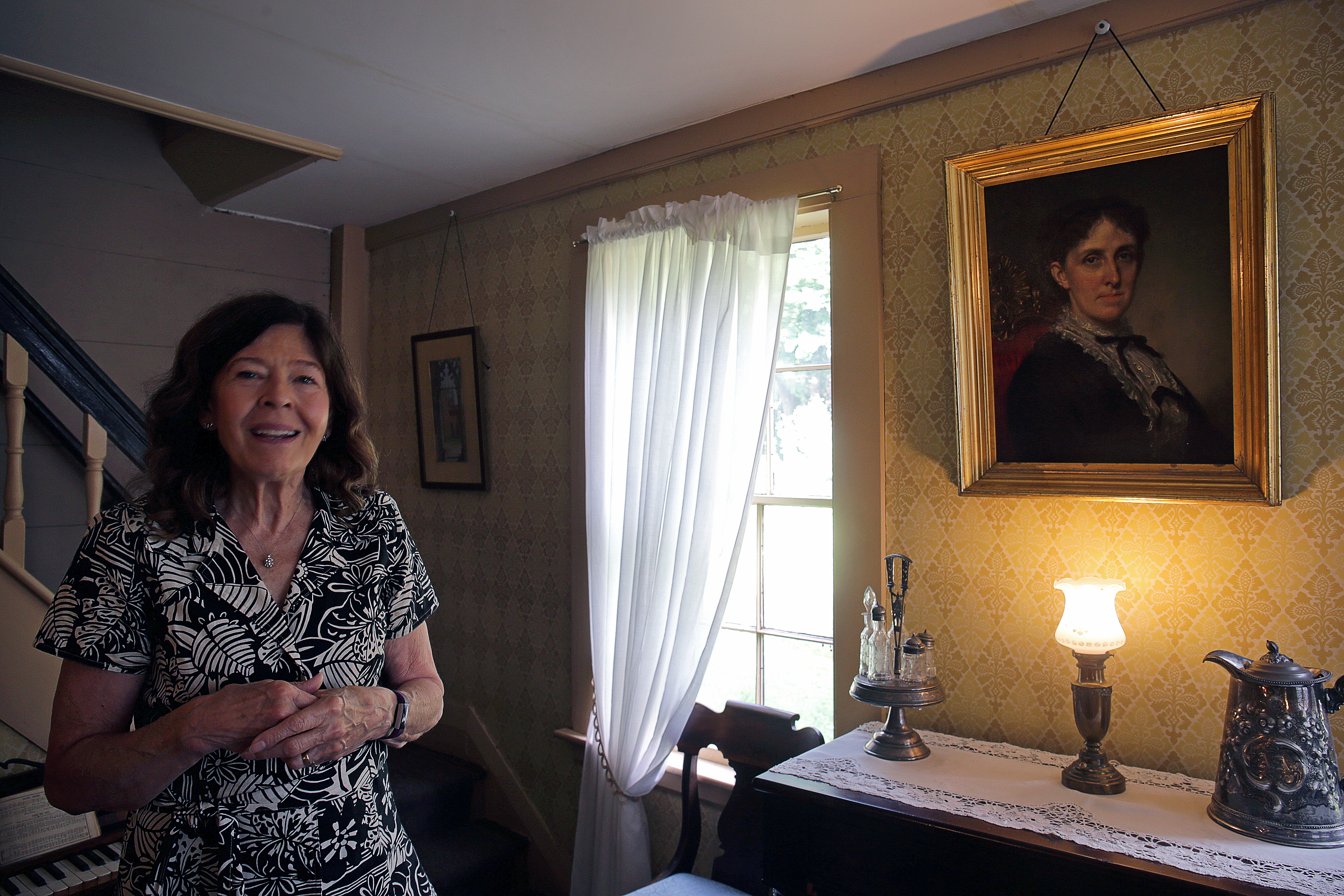Jan Turnquist, executive director of Orchard House, stands next to a portrait of Louisa May Alcott.