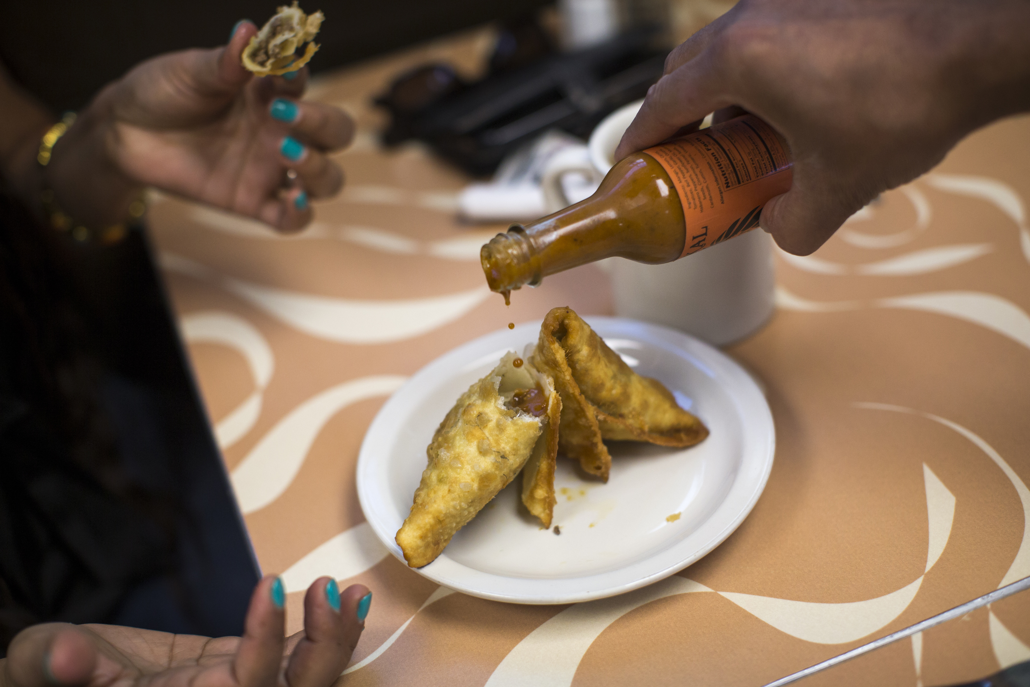 Yahya Noor pours Tawakal's hot sauce on a sambusa.