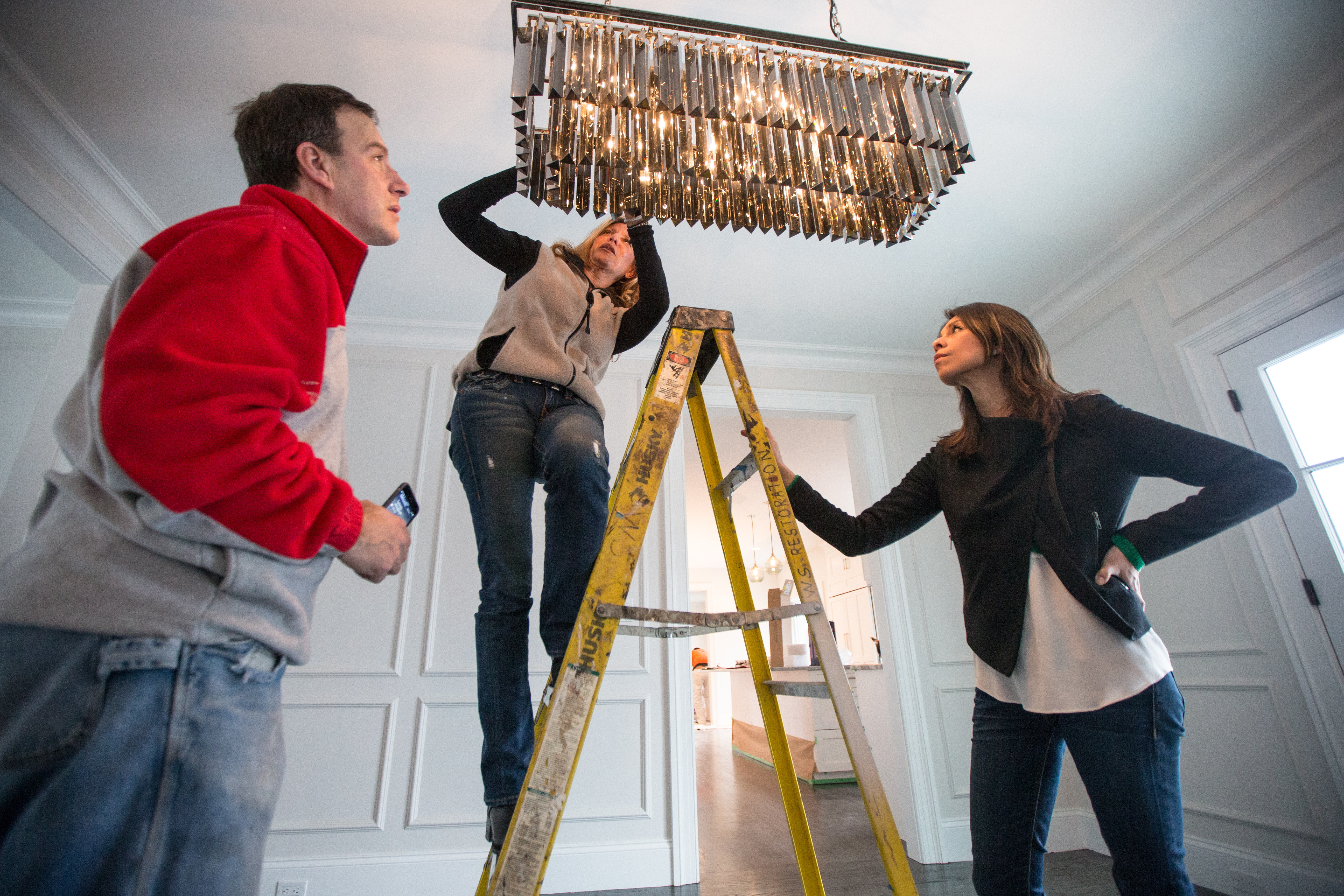 Project manager Glen Sargent (from left), Stumpo, and Almonacid examine a dining room light fixture at the home.