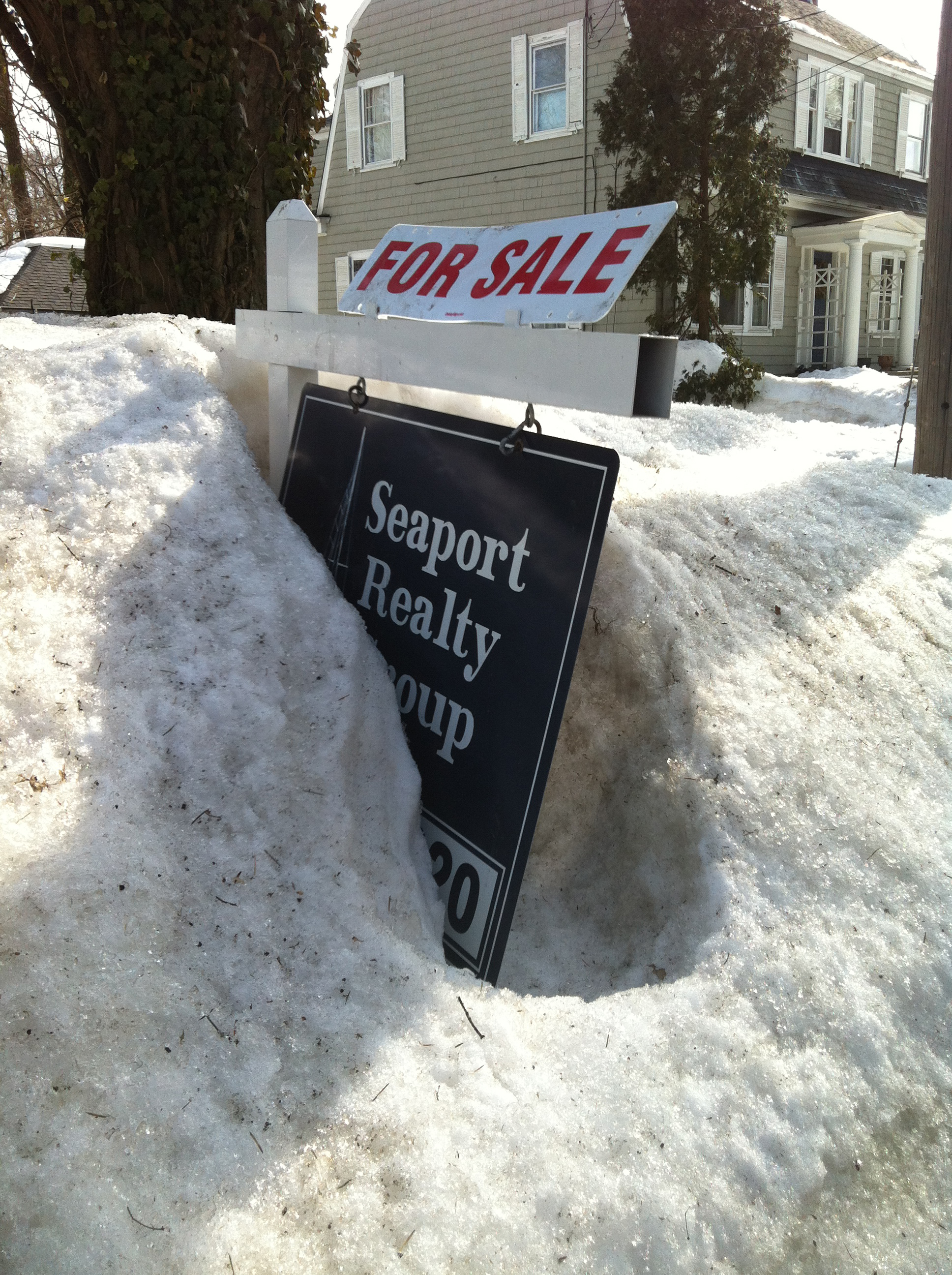 Remnants of this winter’s historic snow obscured this sign on Spafford Road in Milton. Some owners have delayed the listing of their homes until they can clear the driveways or remove ice dams from roofs.
