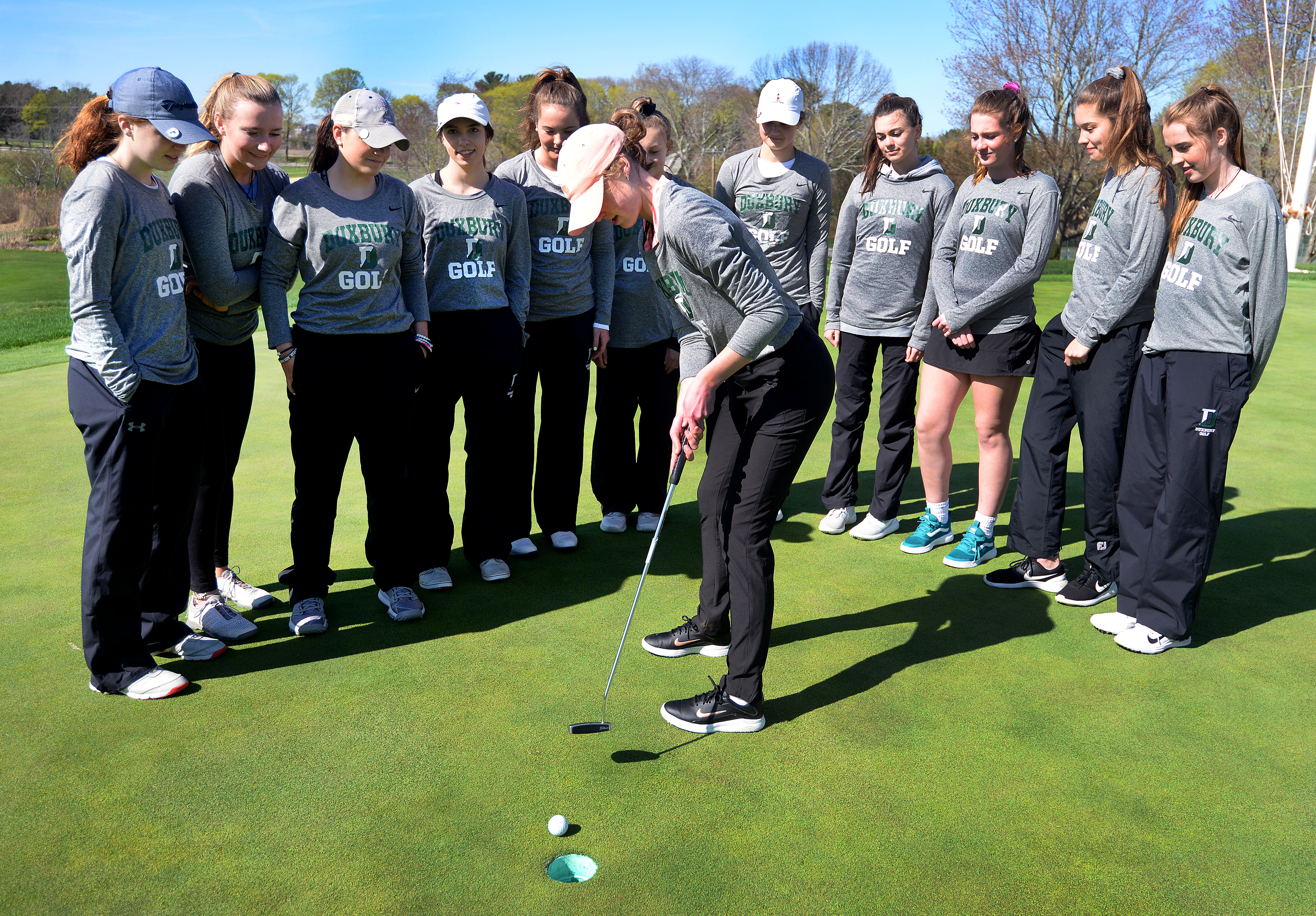The Duxbury girls golf team surrounds Lily Watts as she makes a putt during practice.