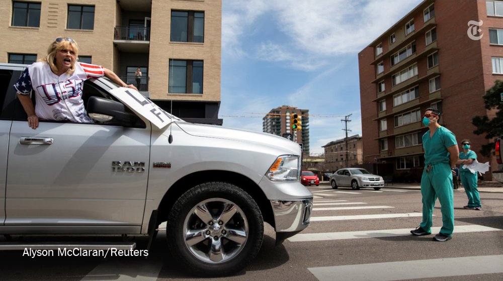 A woman protesting social distancing rules in Denver, Colorado is blocked by a nurse in scrubs.