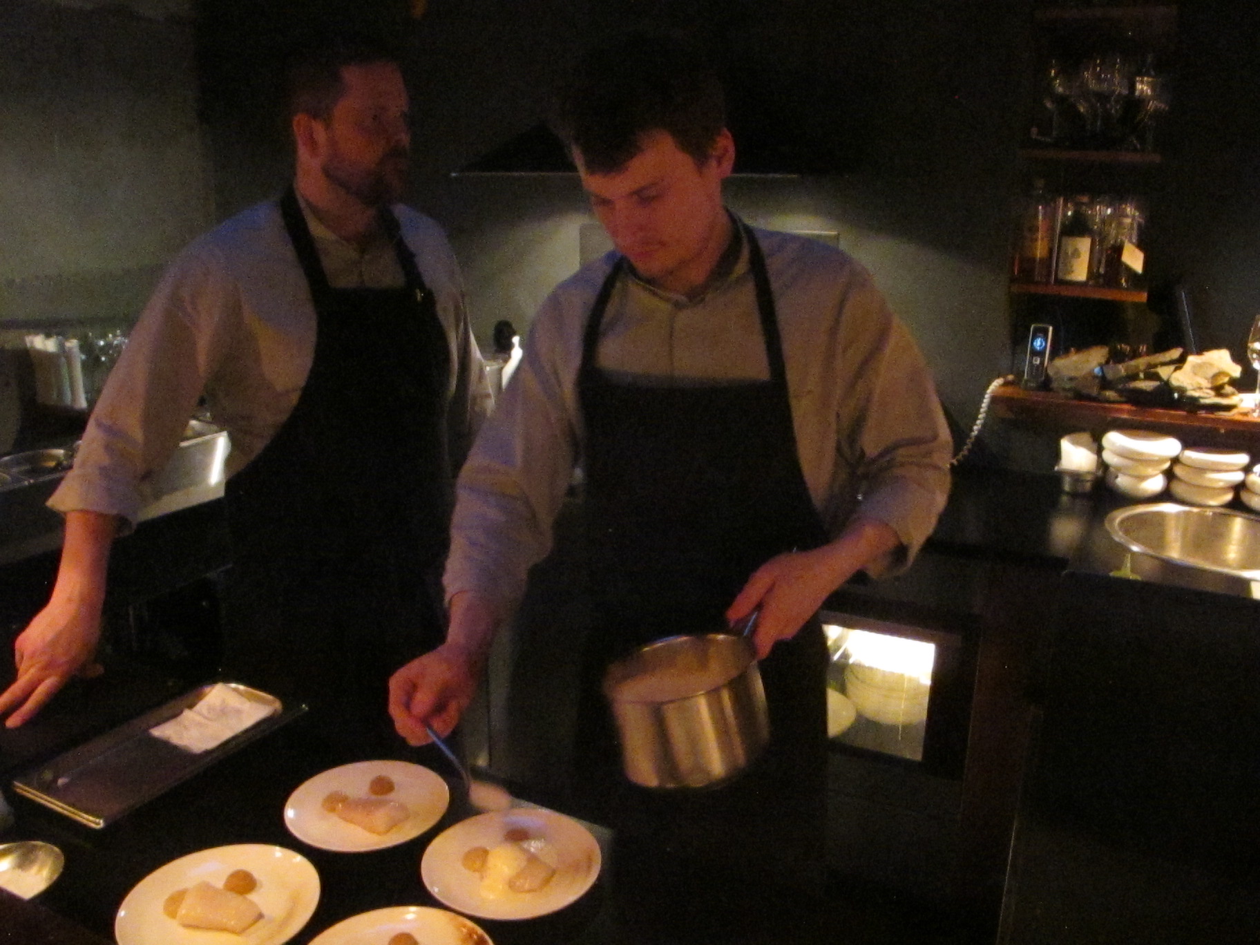 Chefs prepare meals in a small open kitchen.