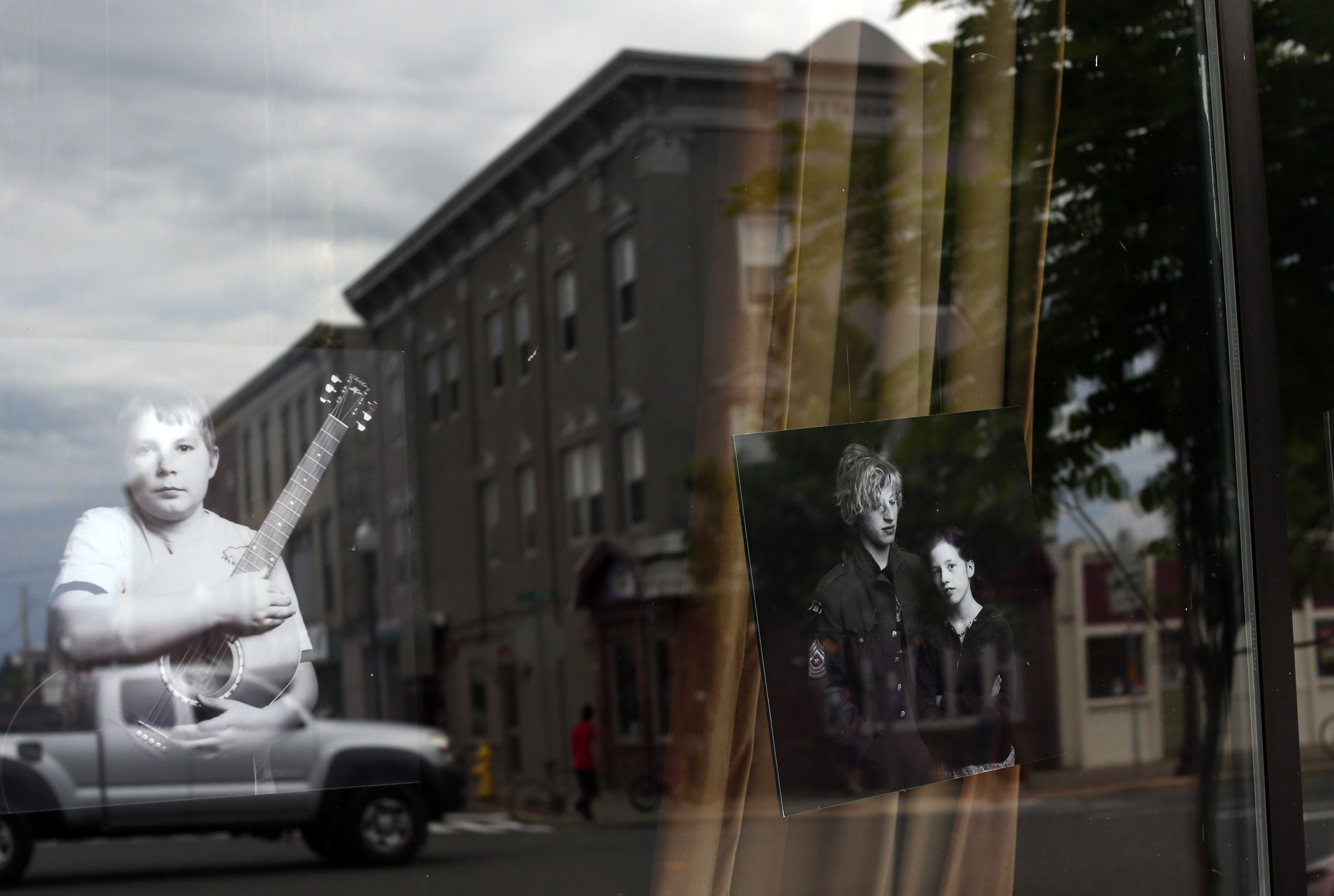 The window of Matt Kim’s Academy of Rock reflects a downtown streetscape of Greenfield.