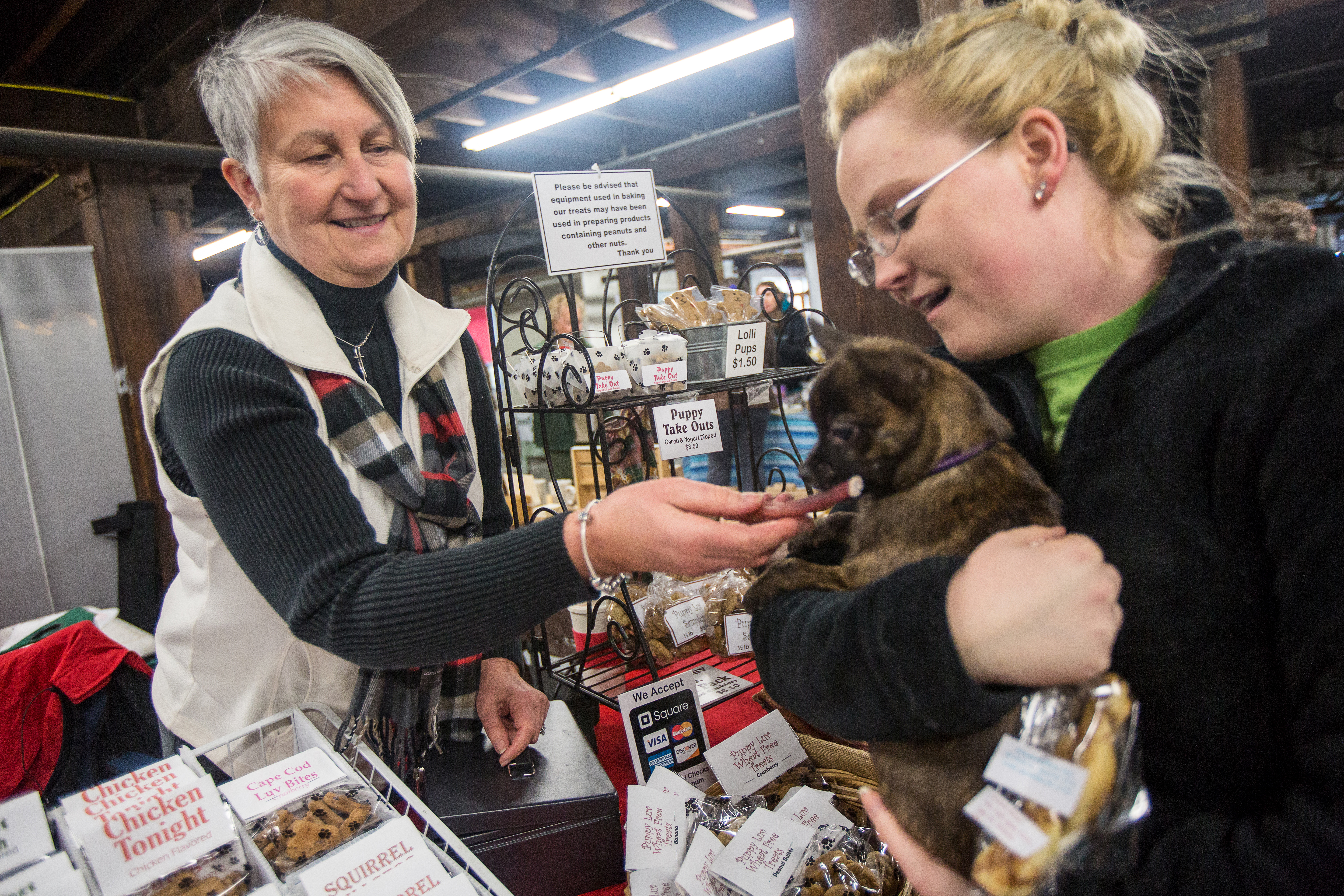 Kathy Varney (left) of Puppy Luv, gives one of her treats to Briana Auclair's dog Gizmo at the Easton Winter Farmers Market at Simpson Spring in Easton.